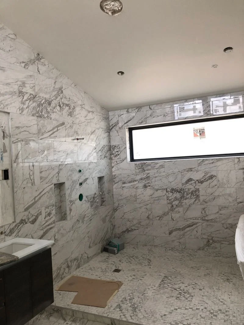 Bathroom under construction with marble walls and floor, a window, and plumbing fixtures installed.