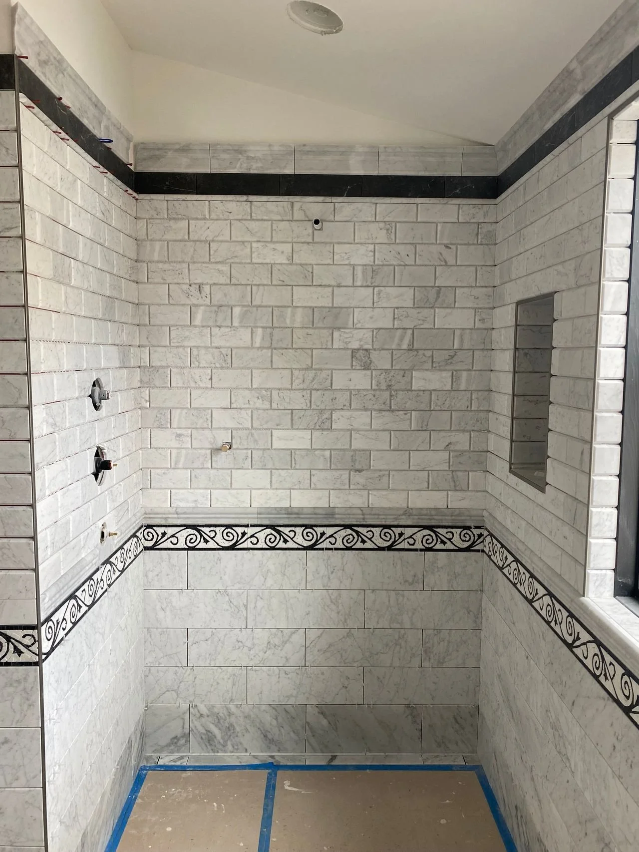 Bathroom with tiled walls, no fixtures installed yet, blue painter's tape on the floor, and a built-in niche.