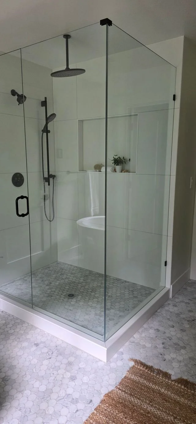 A modern glass-enclosed walk-in shower with black fixtures, a rainfall shower head, a handheld shower wand, and a small window with a potted plant inside.