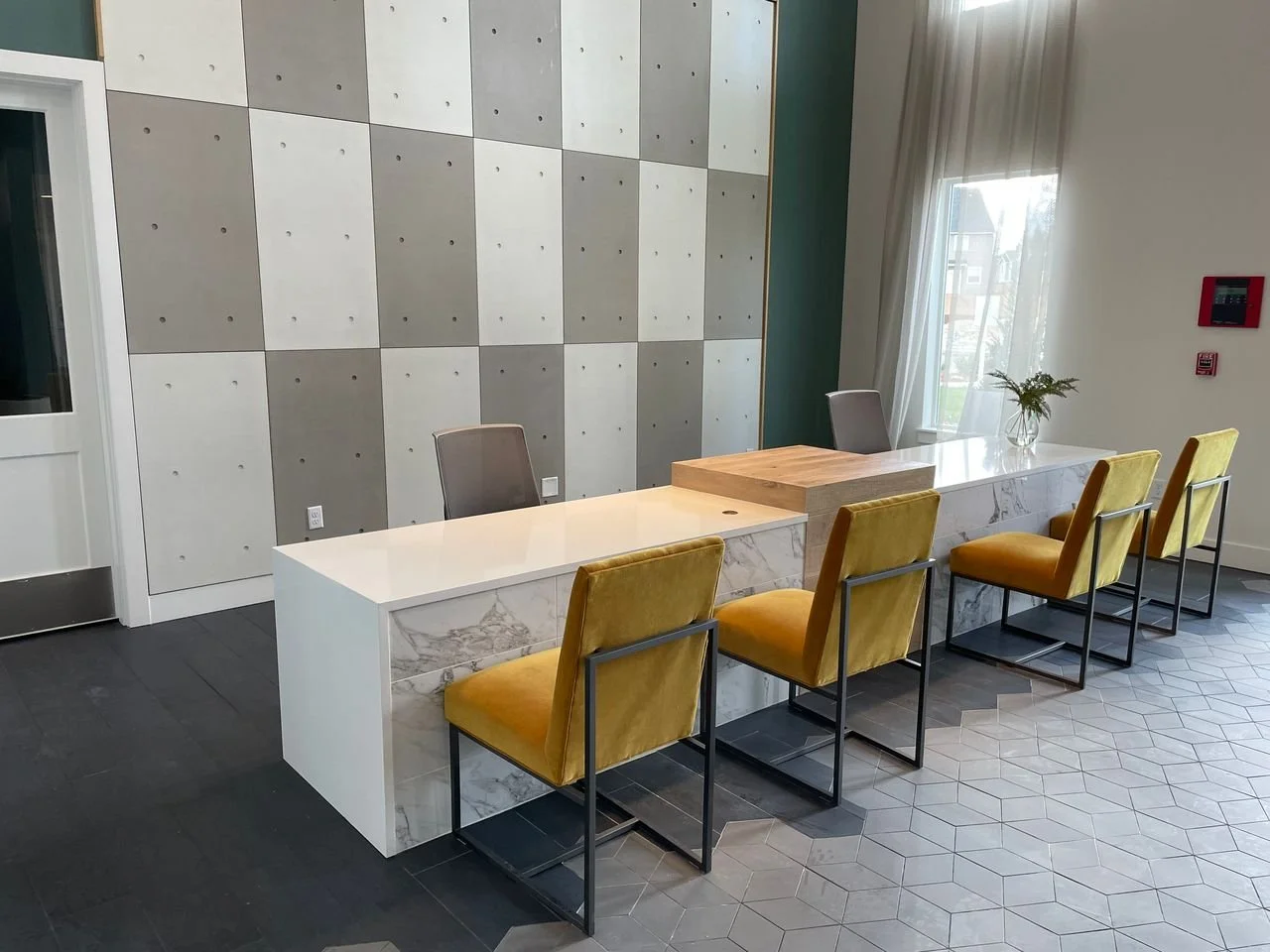 Modern interior space with a white marble table, yellow chairs, and a decorative wall with gray and white panels.