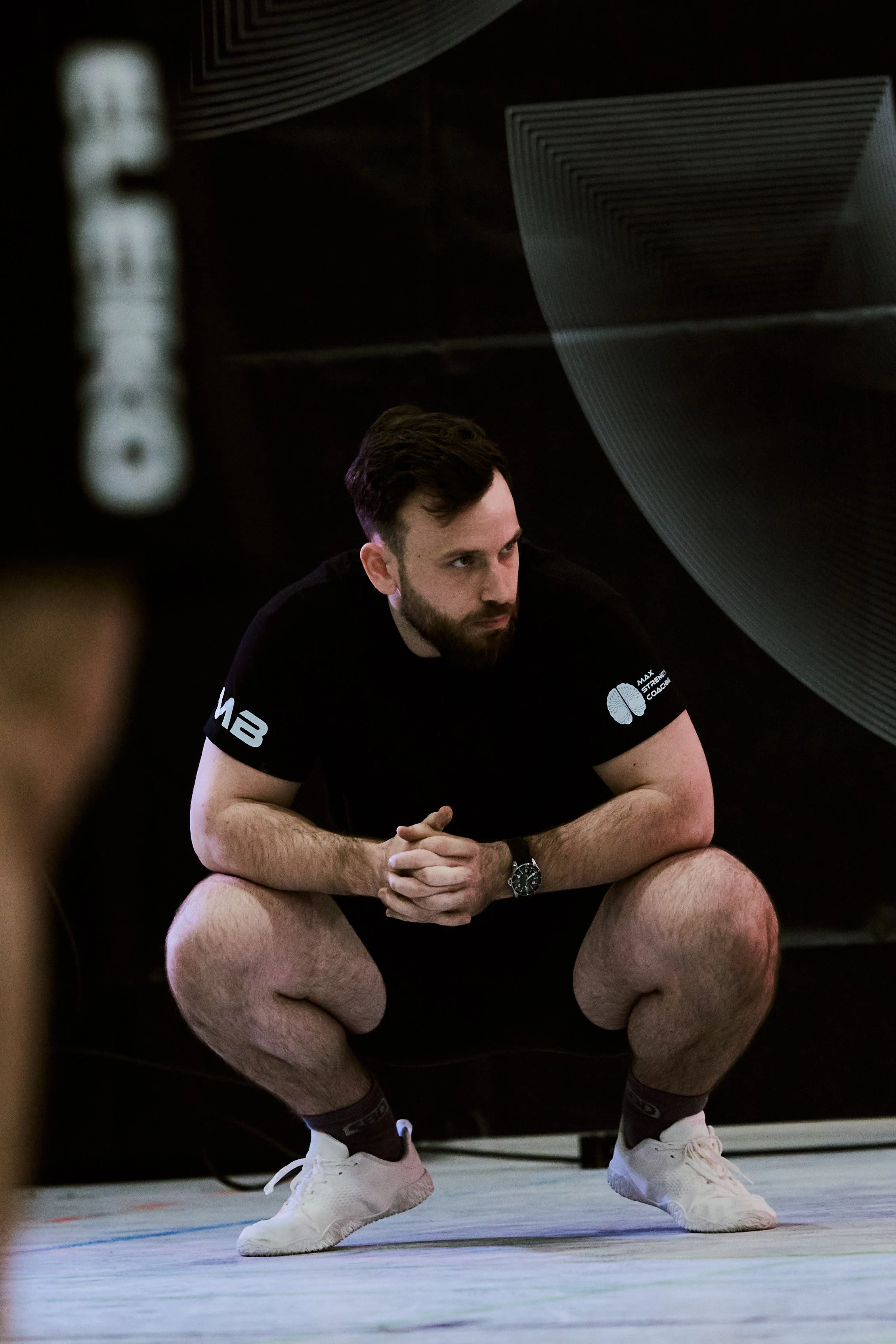 Junger Mann in Sportkleidung, in einer Squashhalle, in einer Hockstellung mit verschränkten Händen, bereit zu spielen.