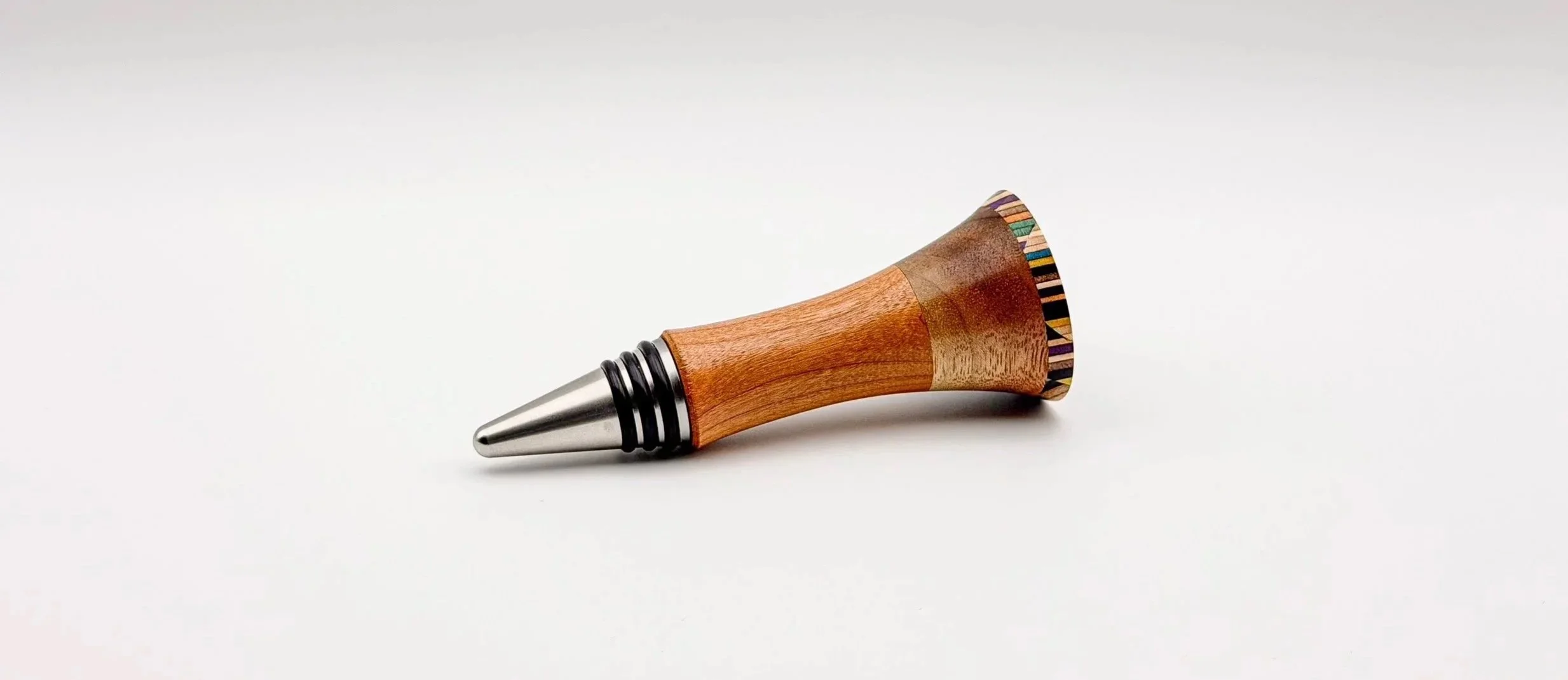 A handcrafted bottle stopper made of recycled skateboard and exotic hardwoods. Lying on a plain white surface.