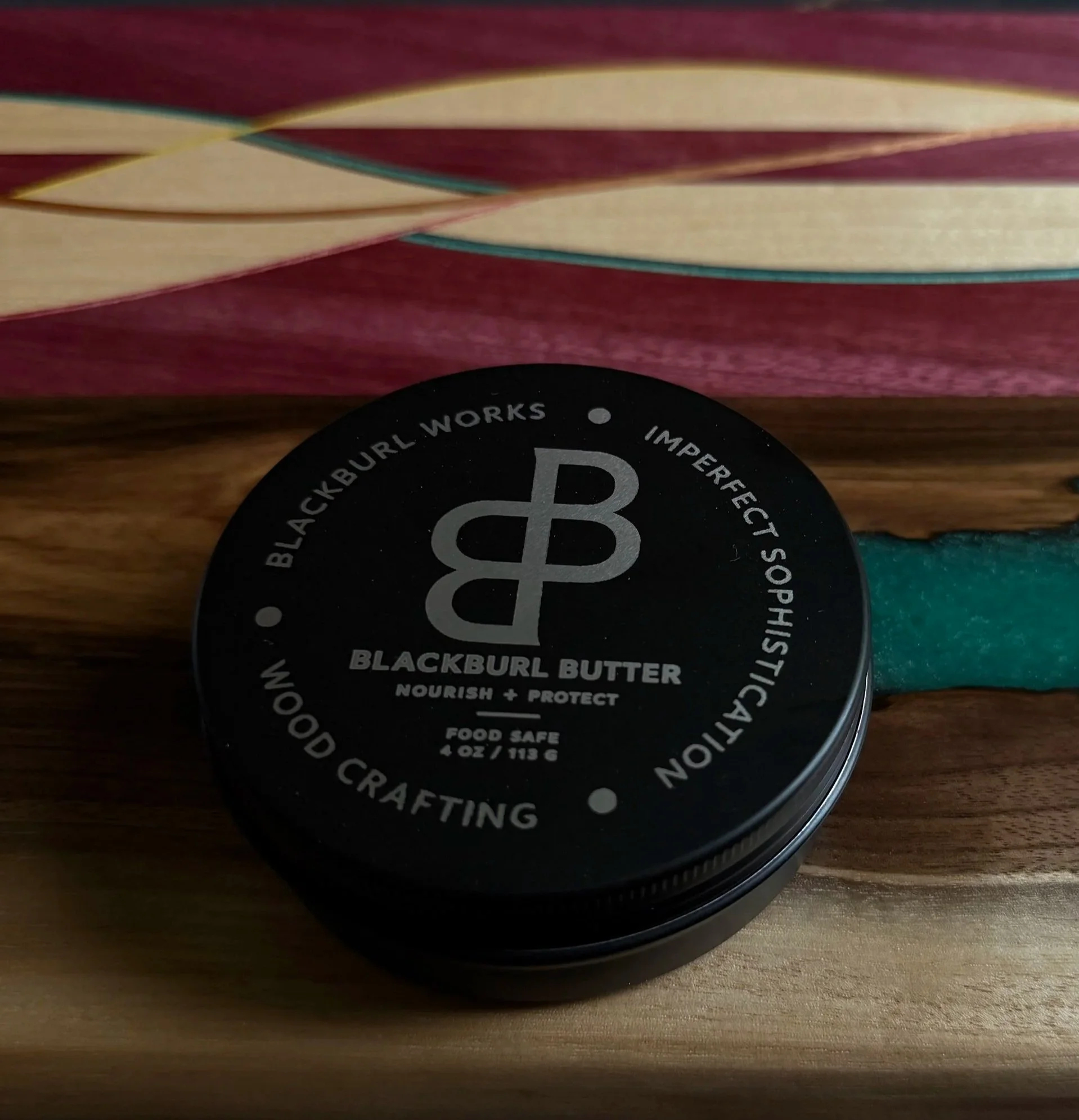 Blackburl Butter food-safe wood conditioner displayed on a handcrafted walnut serving board with recycled skateboard inlay at Blackburl Works.