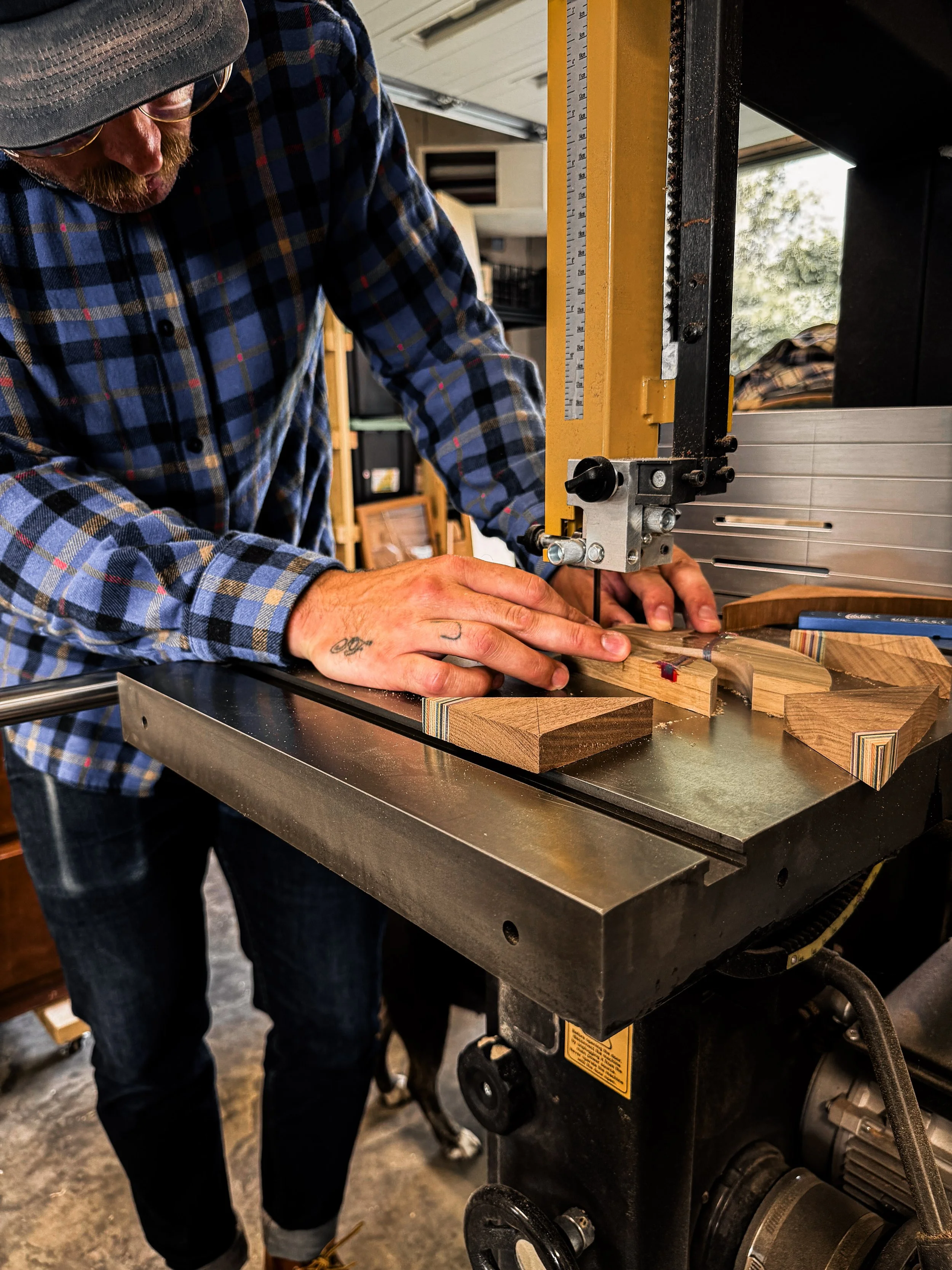A woodworker cutting hardwood and recycled skateboard inlay pieces on a bandsaw during the handcrafted woodworking process.