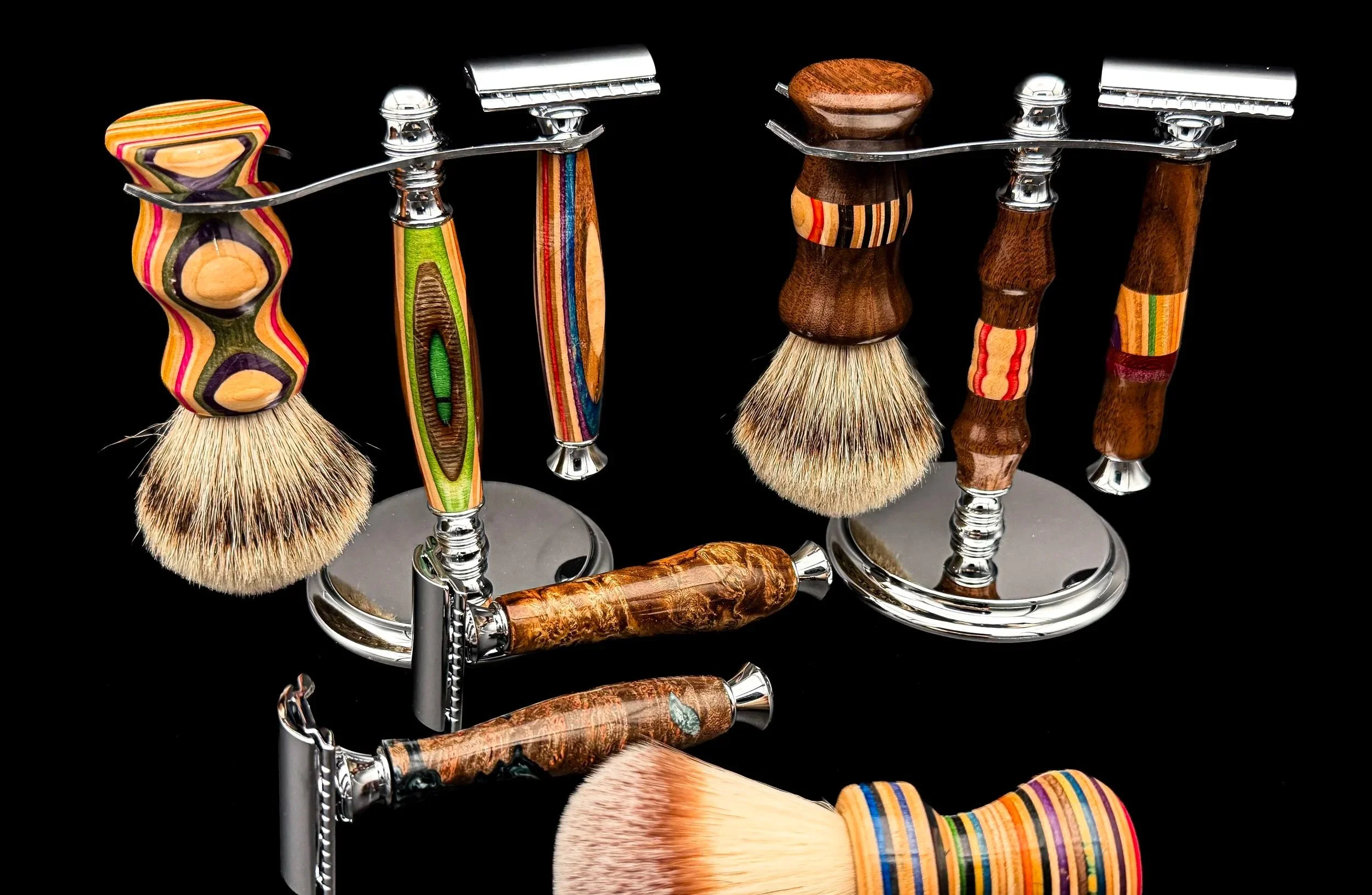 A collection of handcrafted safety razors, shaving brushes, and shaving stands made from premium hardwoods and recycled skateboard materials against a black background.