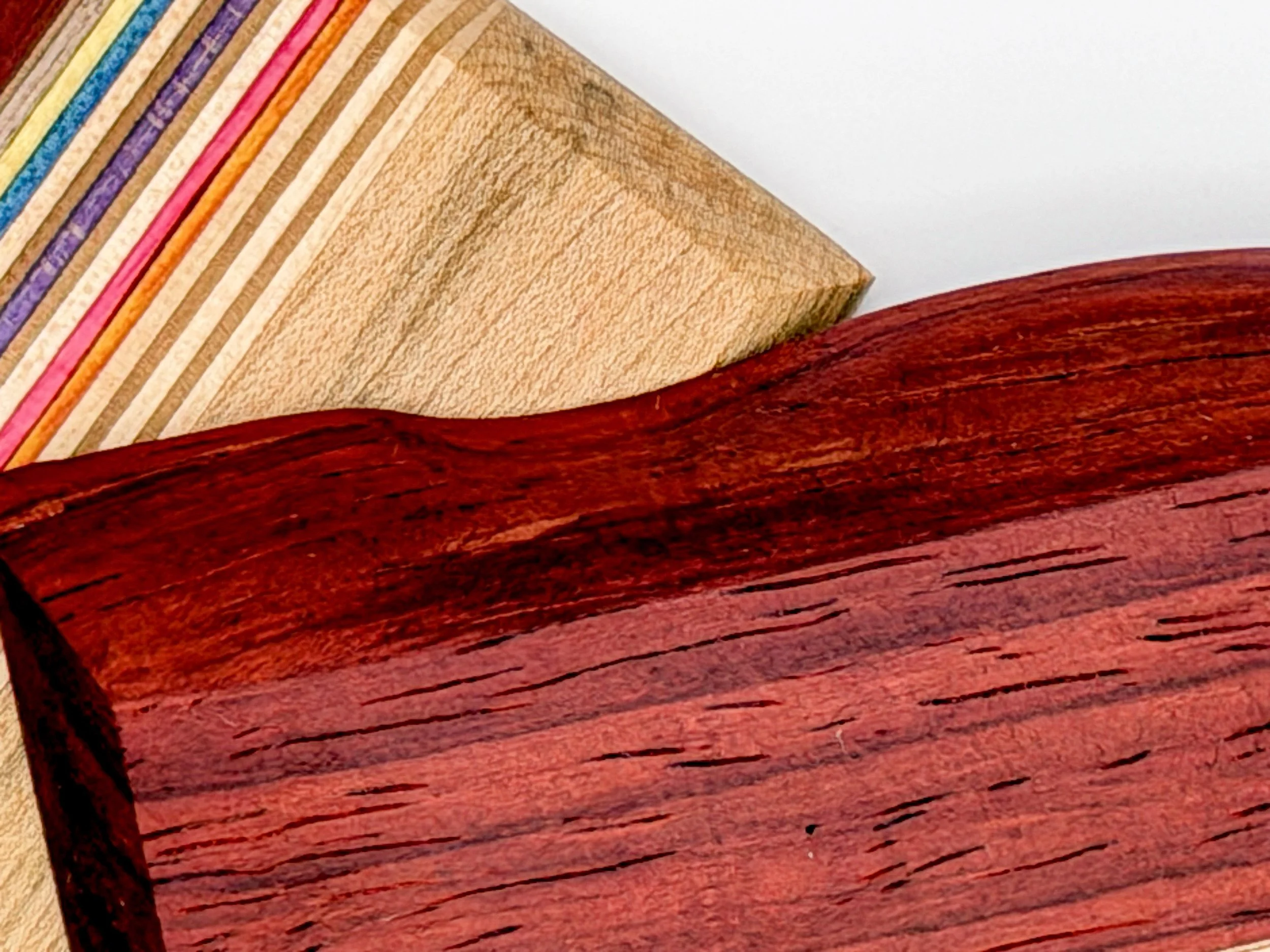 Close-up image of a stack of colorful paper or fabric with the top few edges visible over a polished, reddish-brown wooden surface.