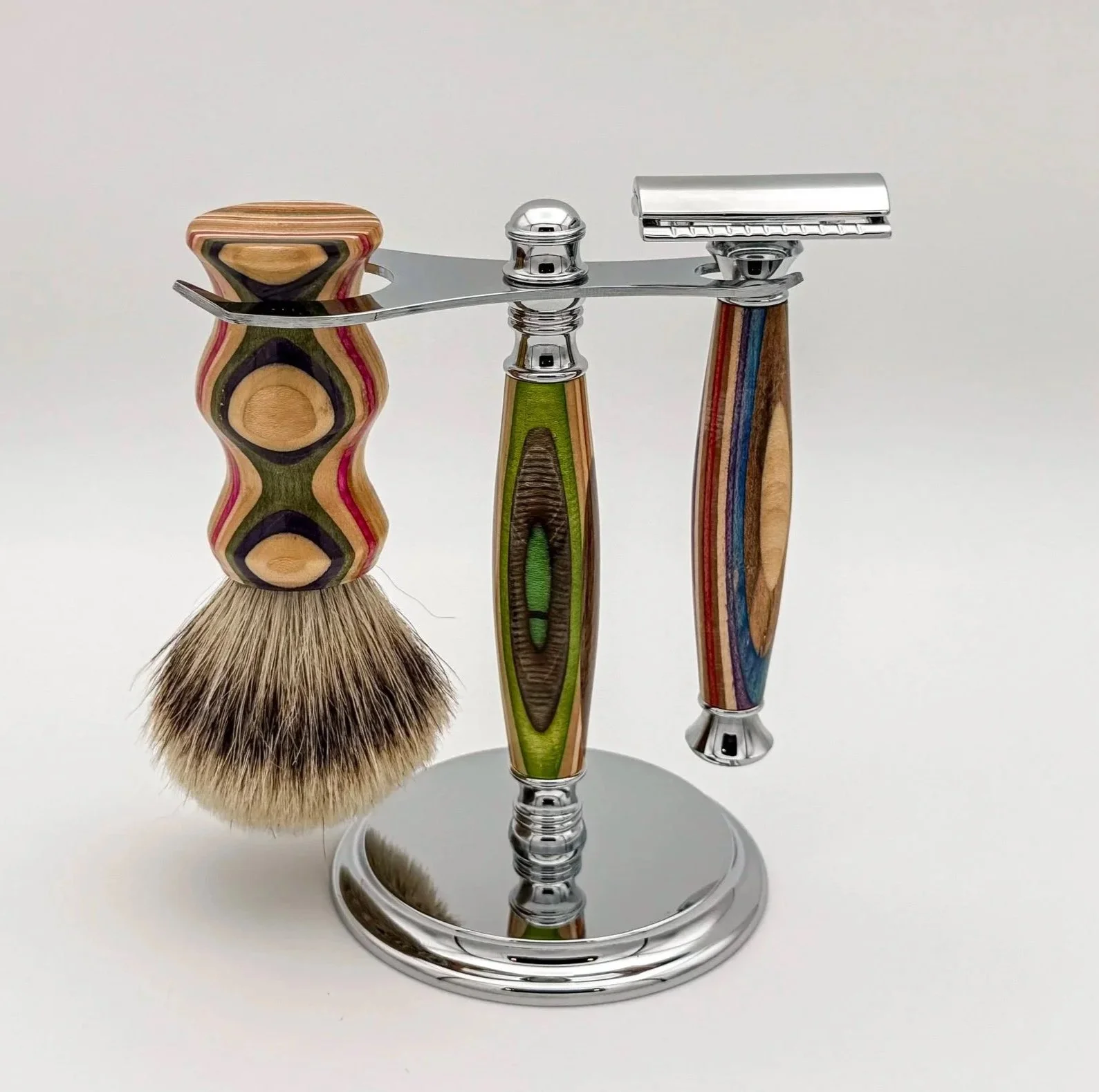 Three safety razors with colorful, patterned handles on a silver stand, one with a shaving brush attached.