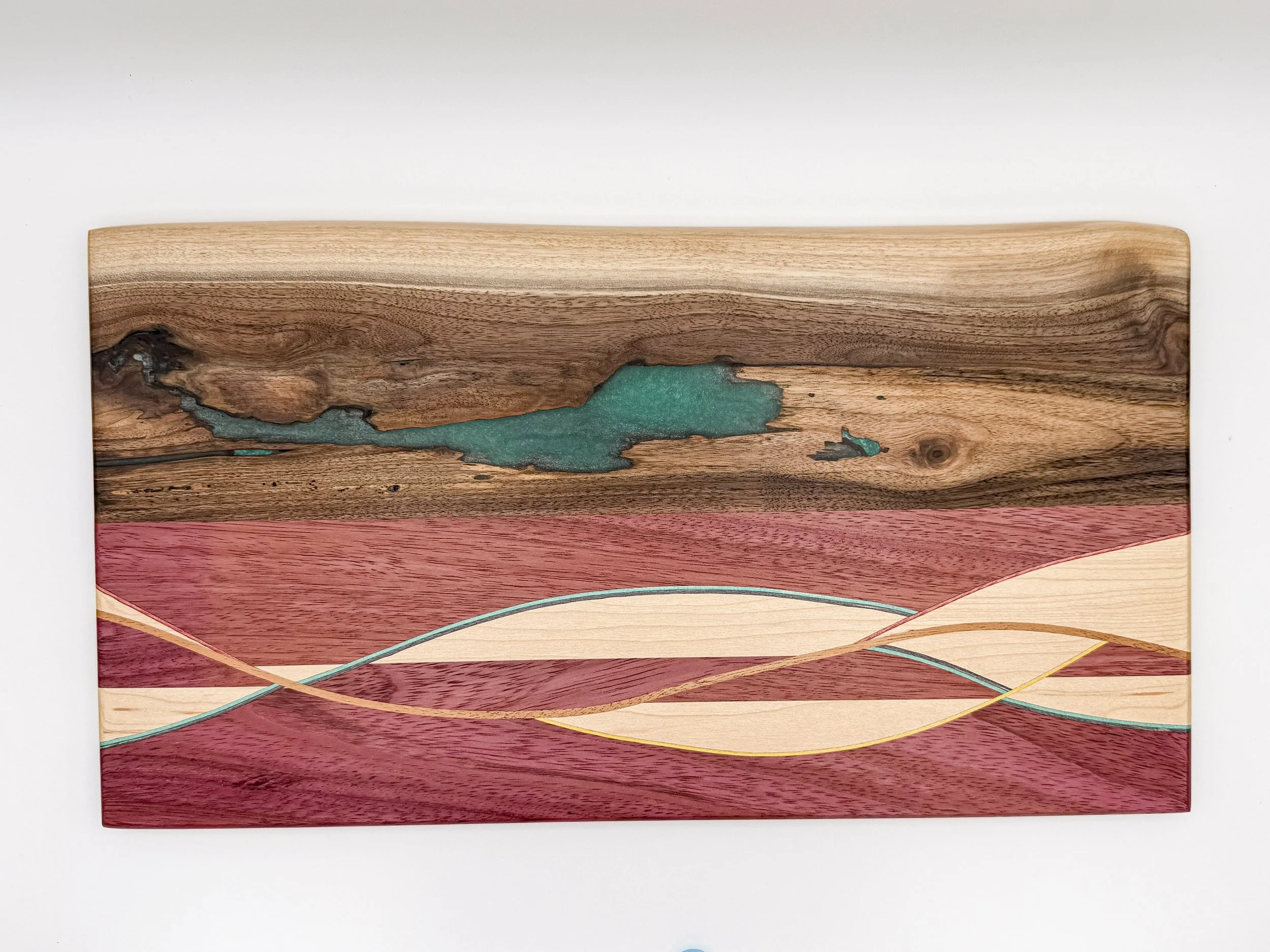 Handmade hardwood serving board featuring a live-edge walnut section, turquoise resin detail, and flowing hardwood inlay by Blackburl Works.