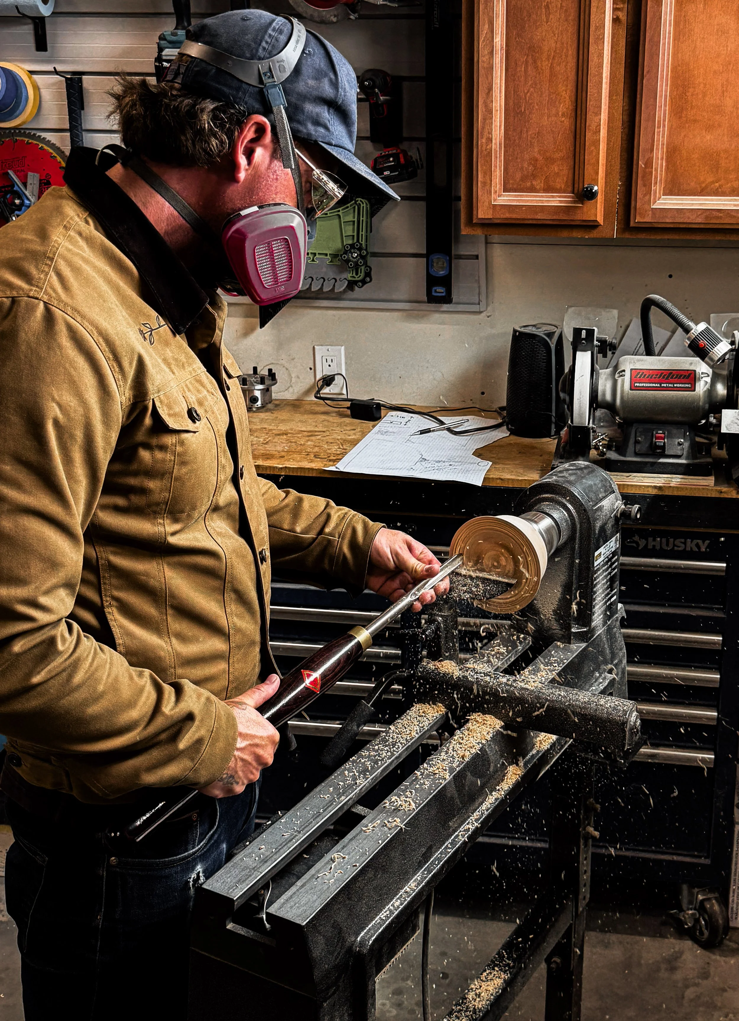 A woodworker wearing protective equipment turns a hardwood bowl on a wood lathe in the Blackburl Works workshop.