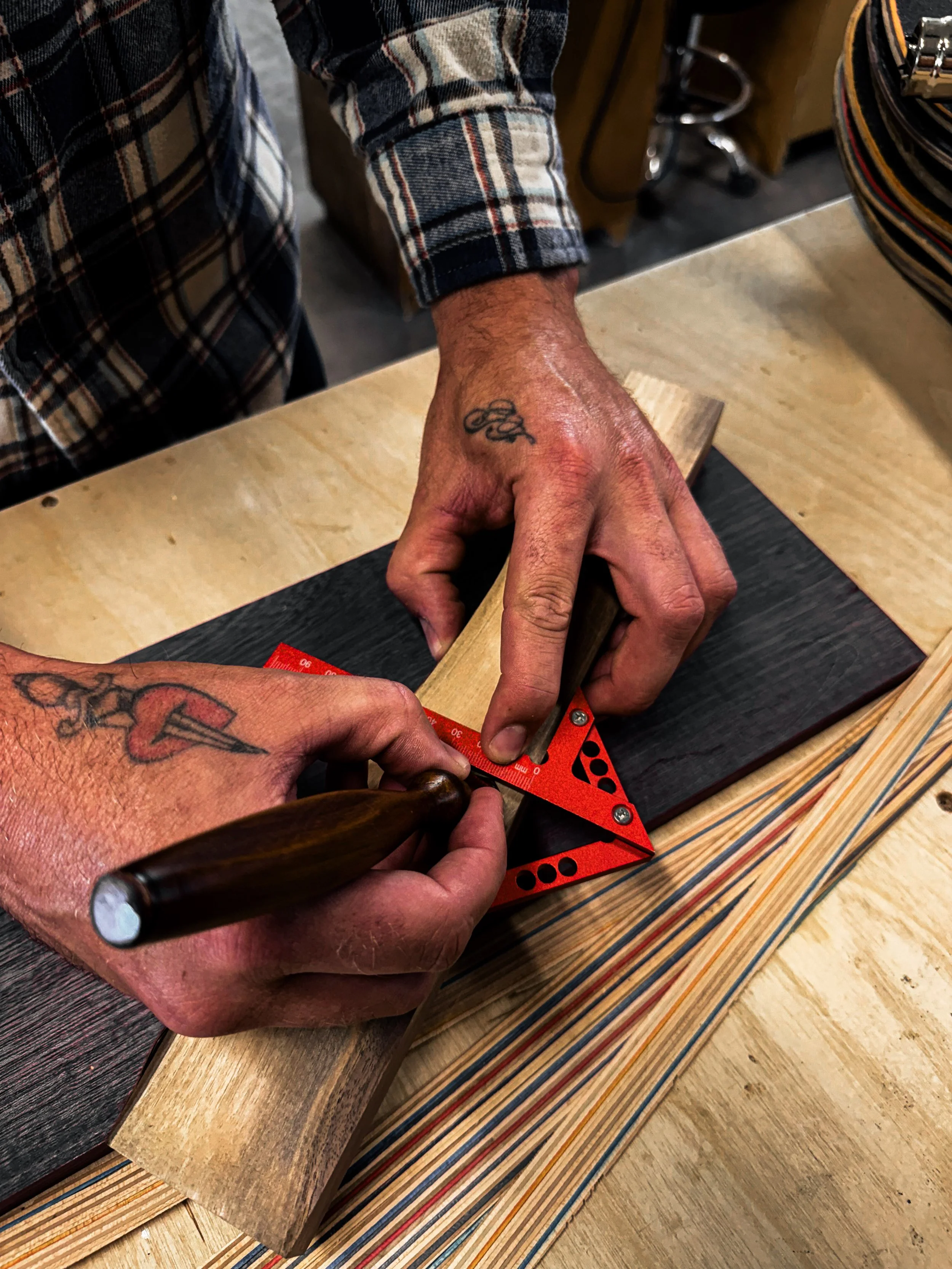 Person measuring a piece of wood with a red triangular ruler in a woodworking shop.