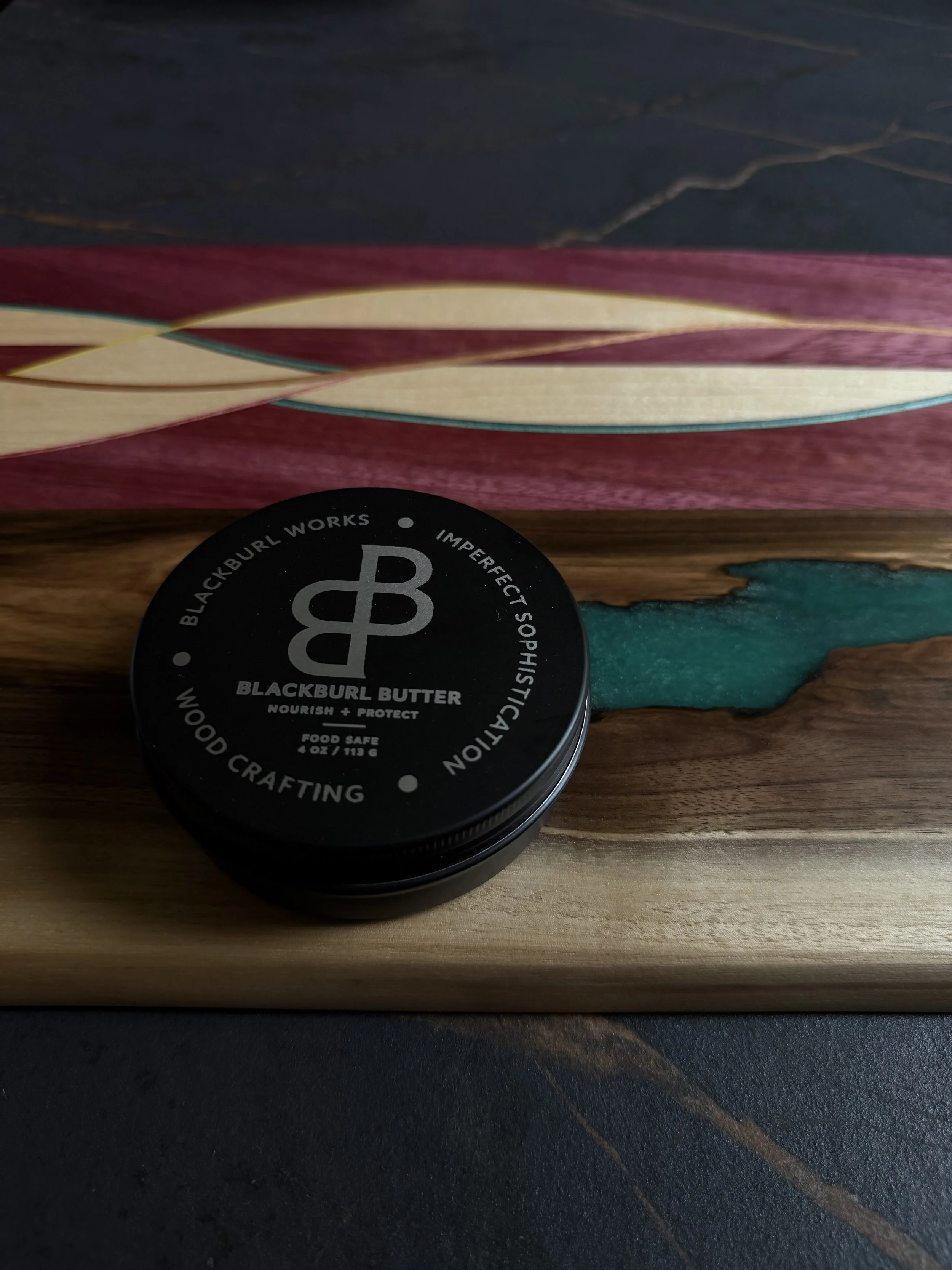 Blackburl Butter food-safe wood conditioner displayed on a handcrafted walnut serving board with recycled skateboard inlay at Blackburl Works.