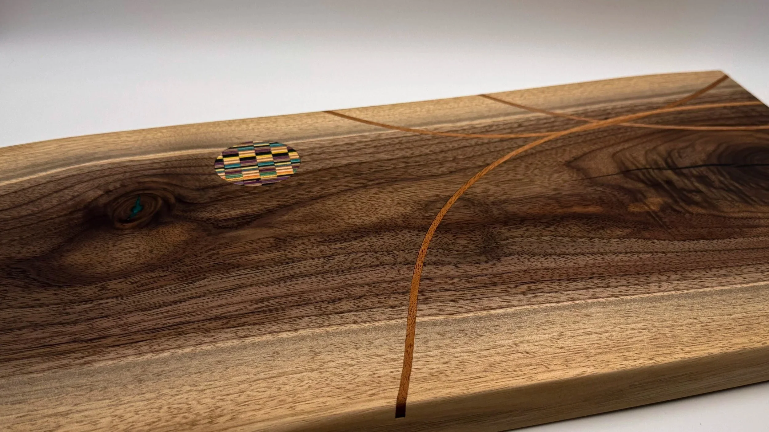 Handcrafted walnut serving board featuring flowing hardwood inlays and a recycled skateboard medallion by Blackburl Works.