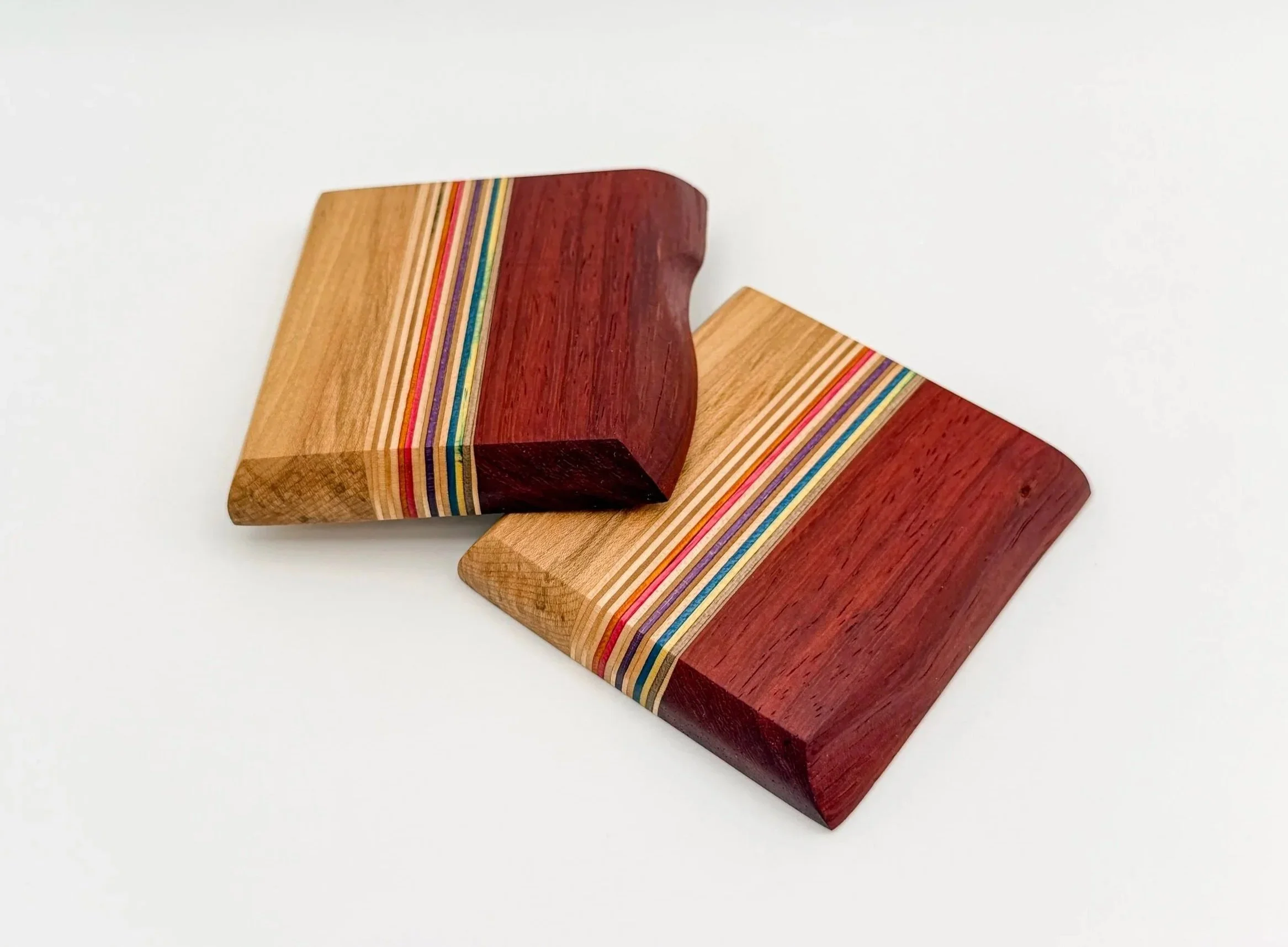 Two wooden coasters amde from recycled skateboards. colourful striped layers on top of each other on a white surface.
