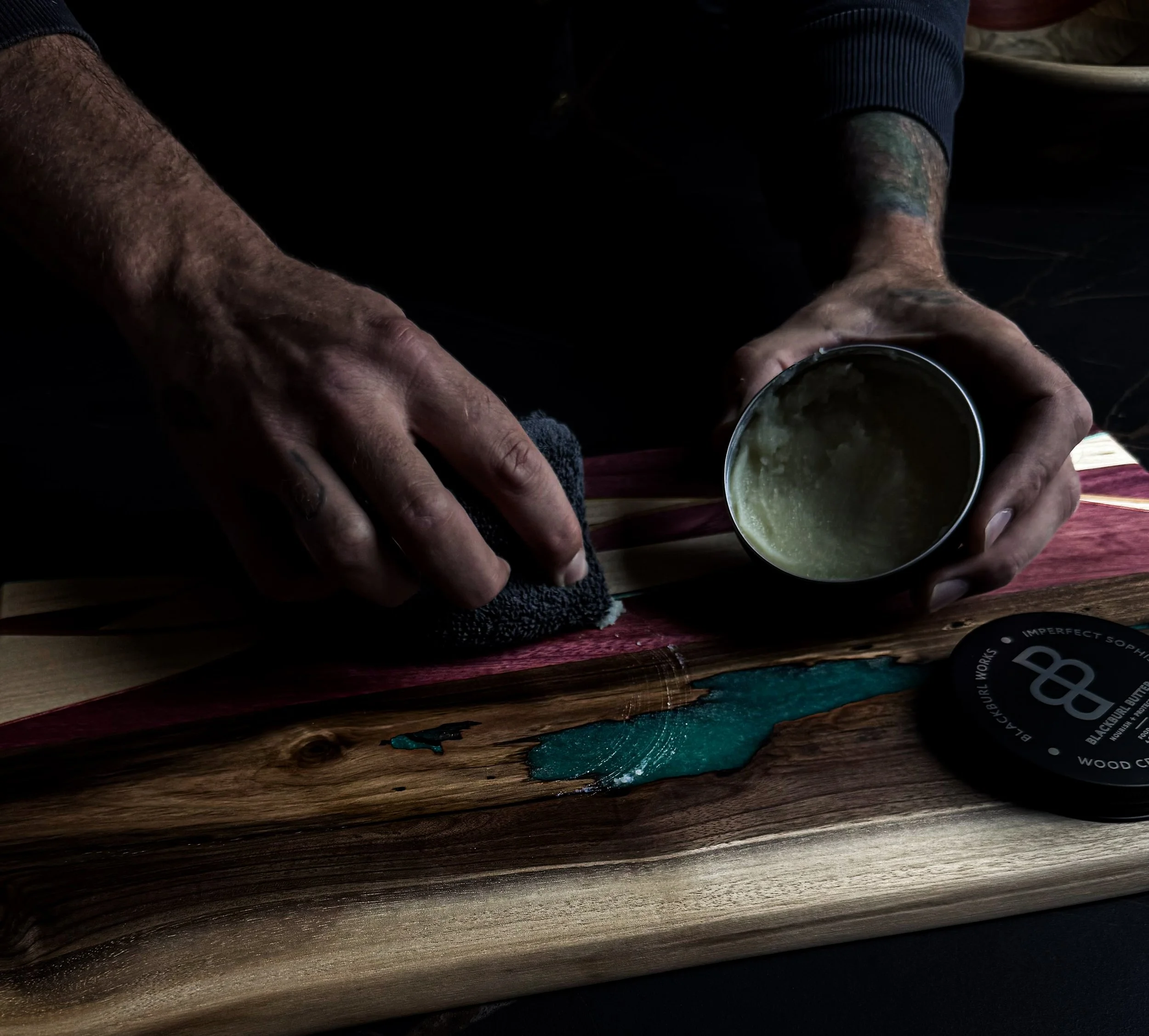 Hand applying Blackburl Butter wood conditioner to a handcrafted walnut serving board with recycled skateboard inlay during the finishing process at Blackburl Works in Fernie, British Columbia, Canada.