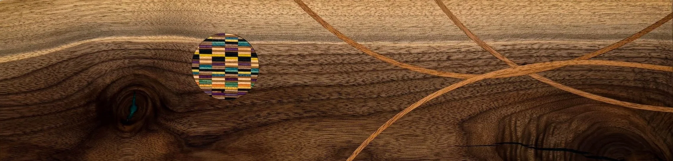Close-up of a wooden surface with knots, a colorful recycled skateboard mosiac inlay, and a few thin mahogony inlays