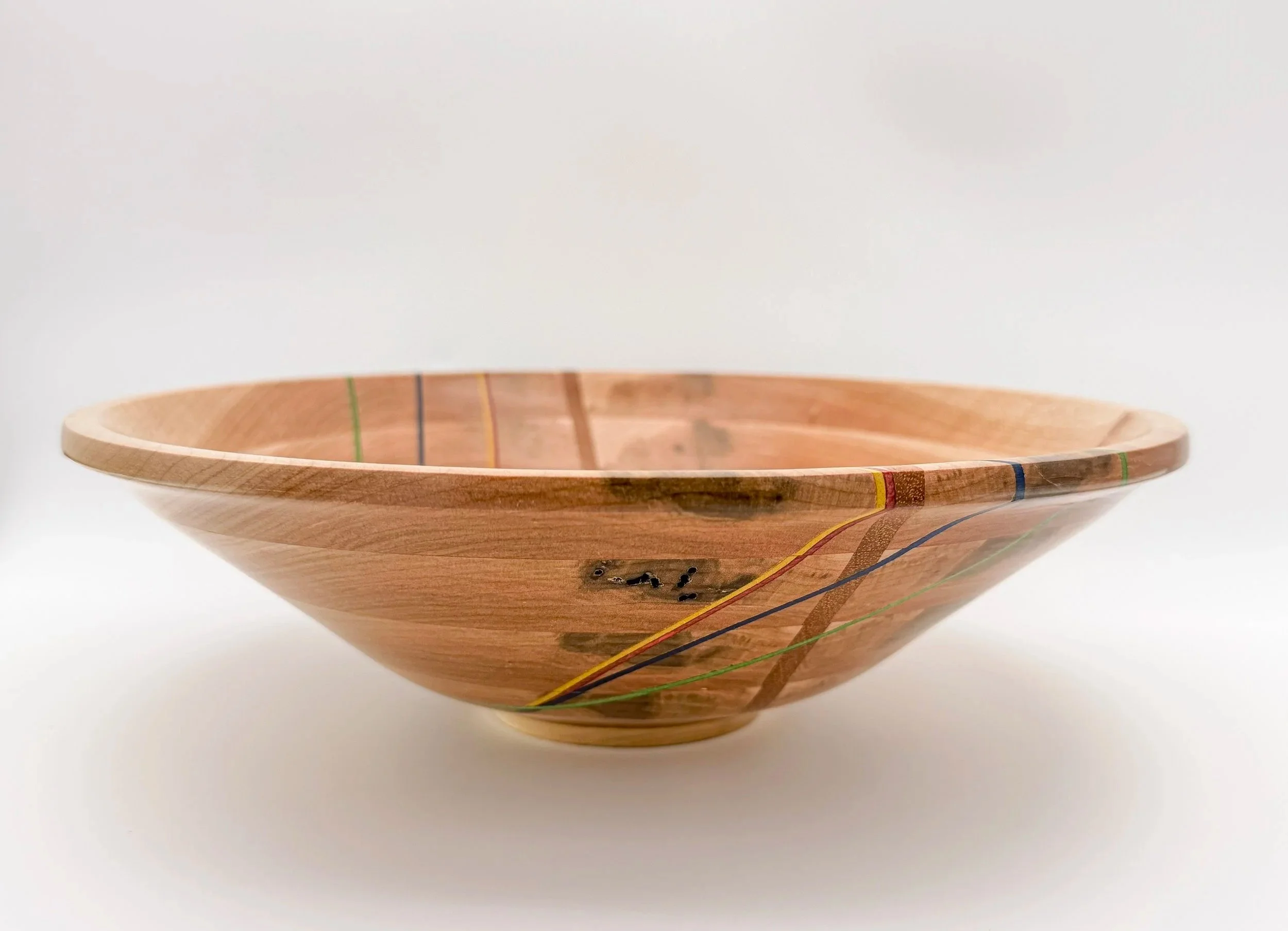 A wooden bowl with a smooth, rounded shape and colorful recycled skateboard veneers  along its outer edge, placed on a plain white background.