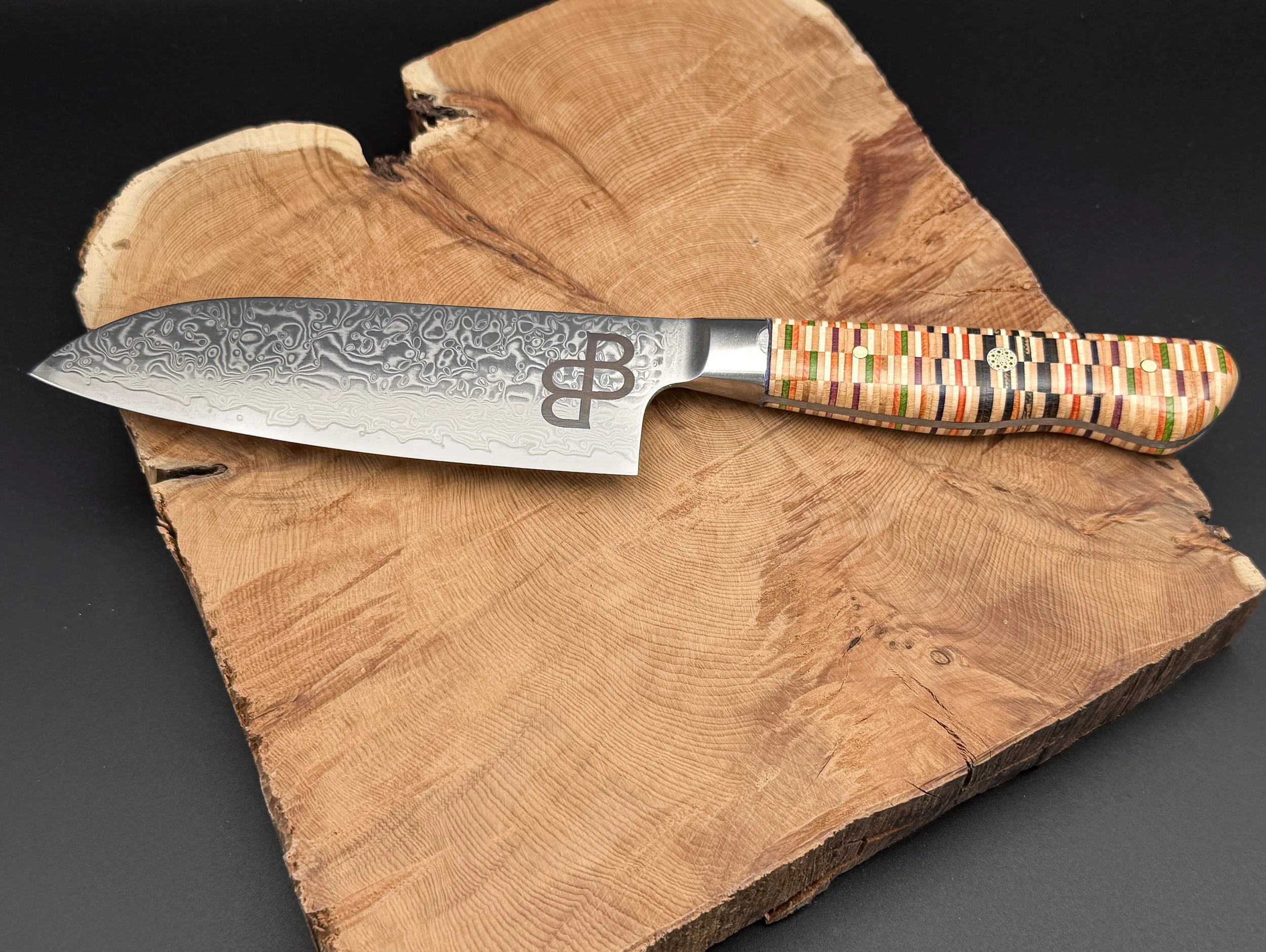 Close-up of a Japanese Damascus steel  kitchen knife with a recycled skateboard handle resting on a wooden cutting board.
