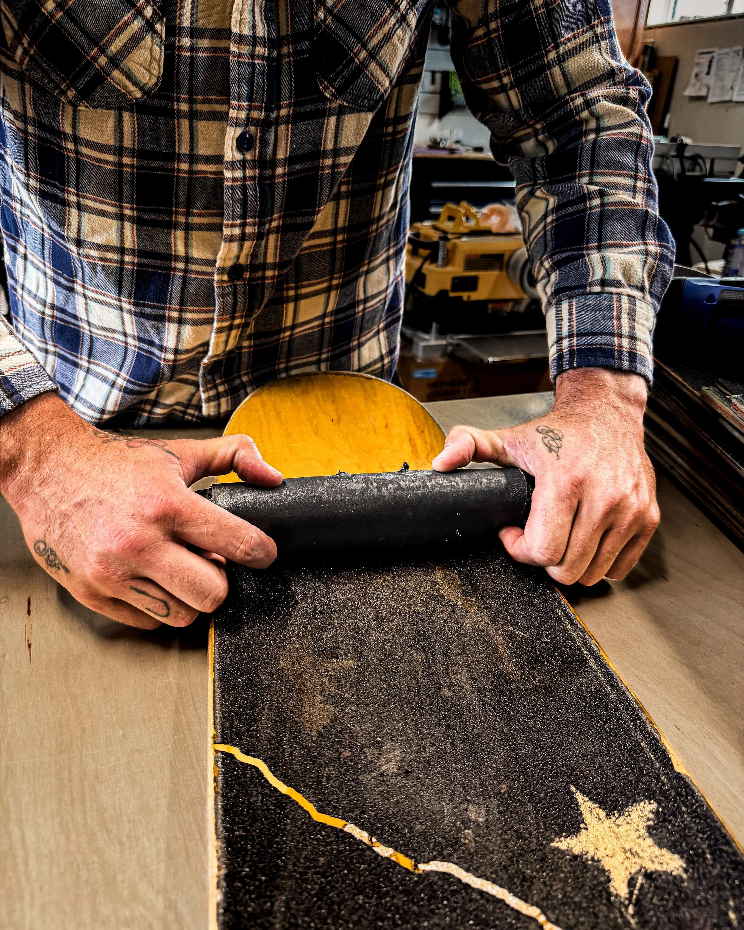 Hands removing grip tape from a recycled skateboard deck before transforming it into a handcrafted wood product in the Blackburl Works workshop.