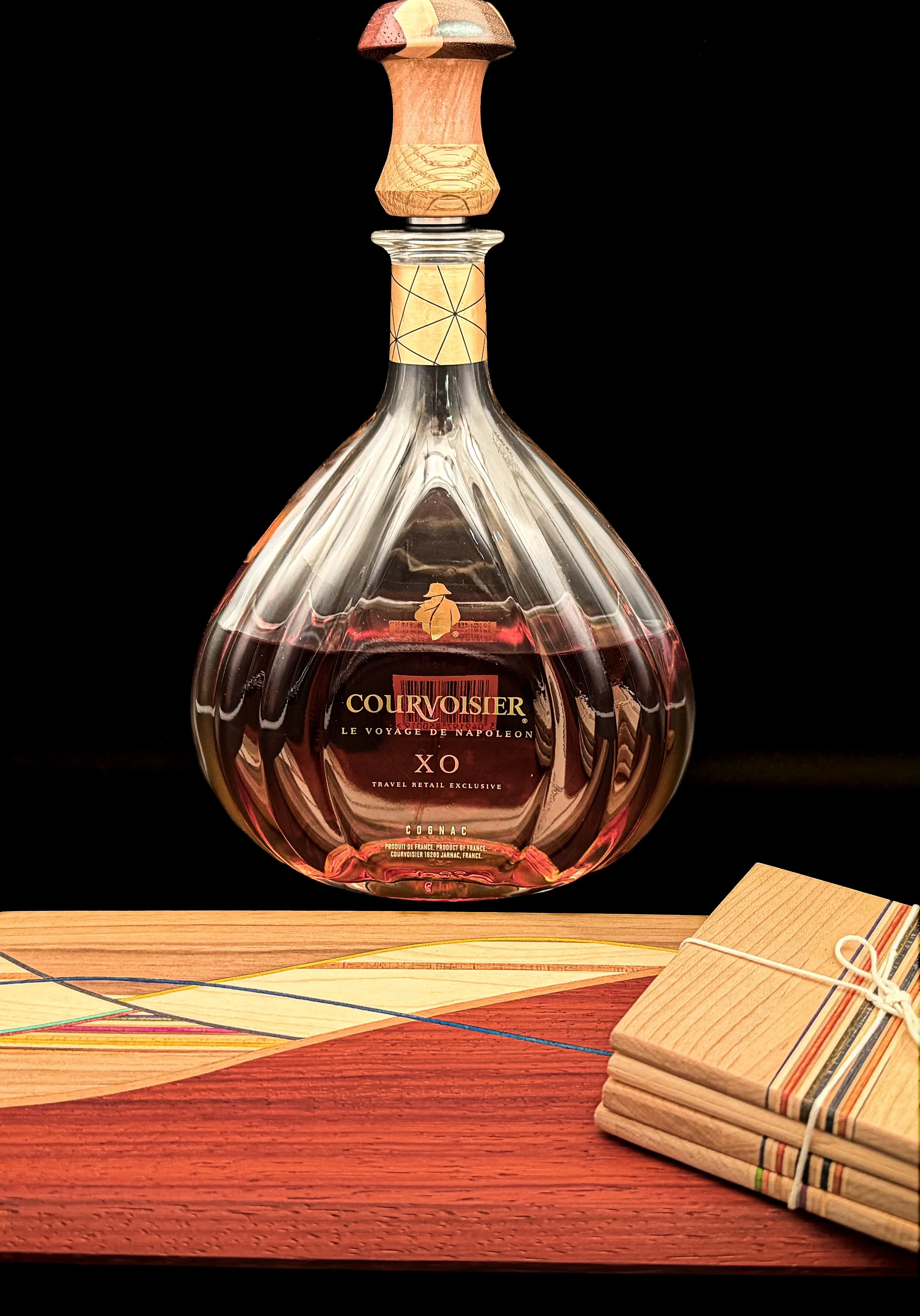 Handcrafted hardwood bottle stopper displayed in a crystal spirits decanter alongside handcrafted hardwood coasters by Blackburl Works in Fernie, British Columbia, Canada. Made from premium hardwoods with signature geometric detailing, each one-of-on