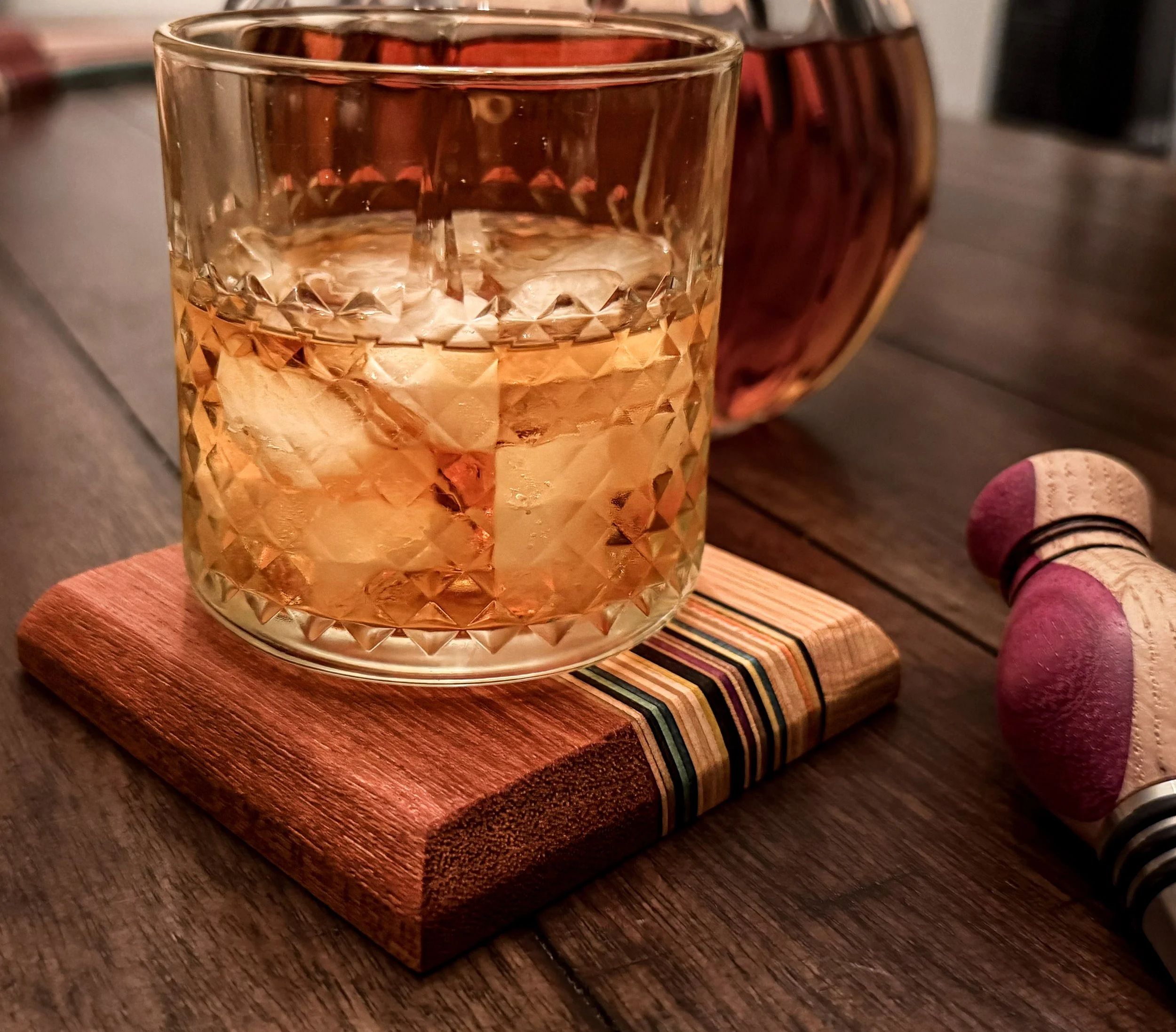 A glass of whisky on a wooden coaster, placed on a wooden surface. made from hardwood and recycled skateboards