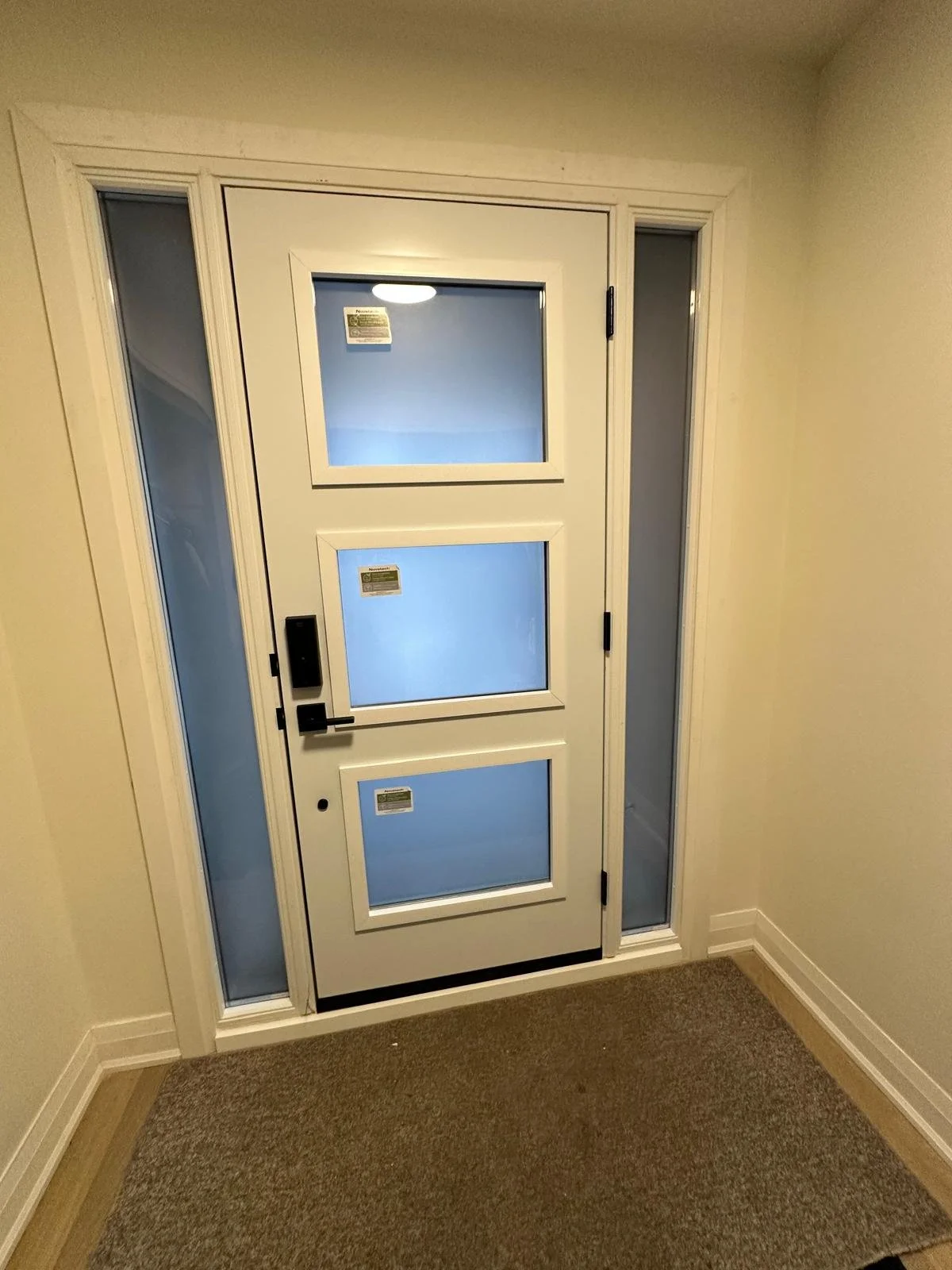 Residential front door with three small windows, side panels with glass, and a black handle and lock