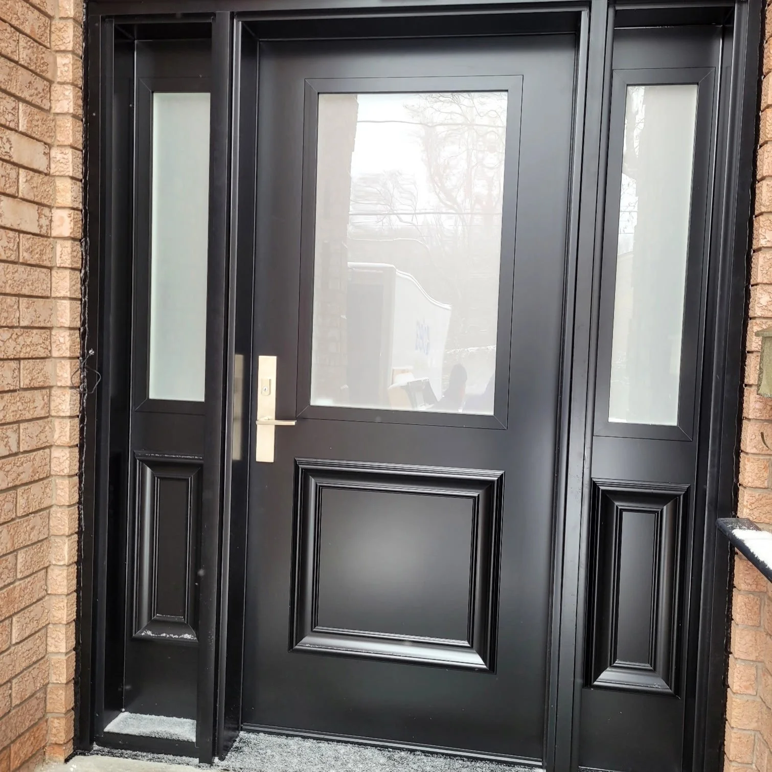 Black front door with large glass panel and sidelights, set in brick wall