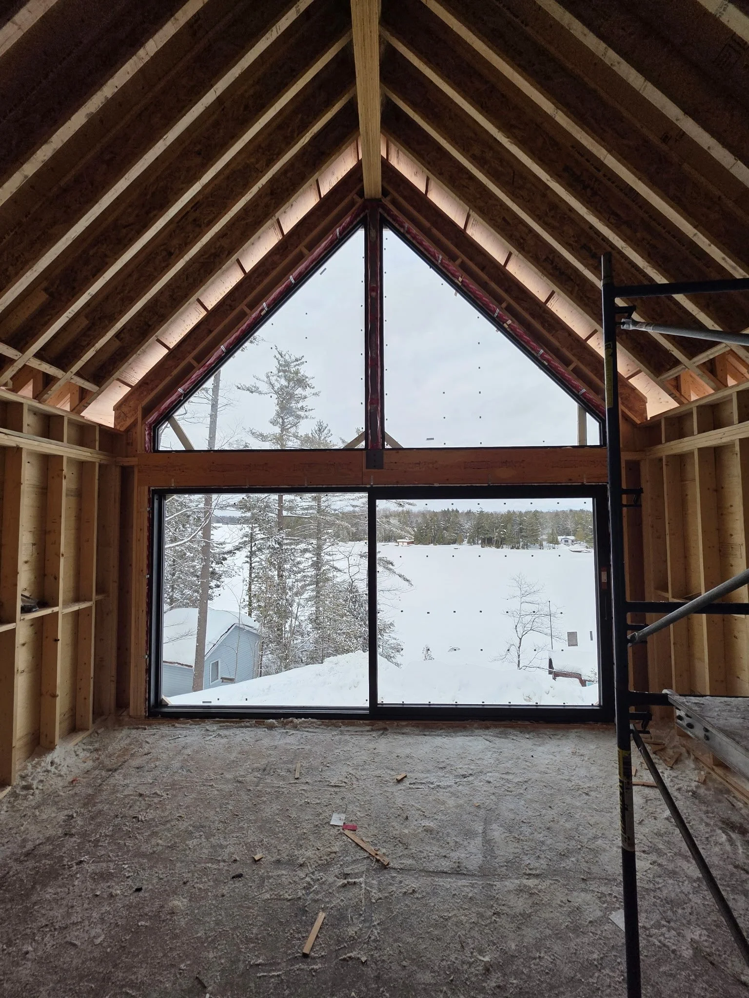 View from inside a house under construction, showing large triangular and rectangular windows with snowy landscape outside.