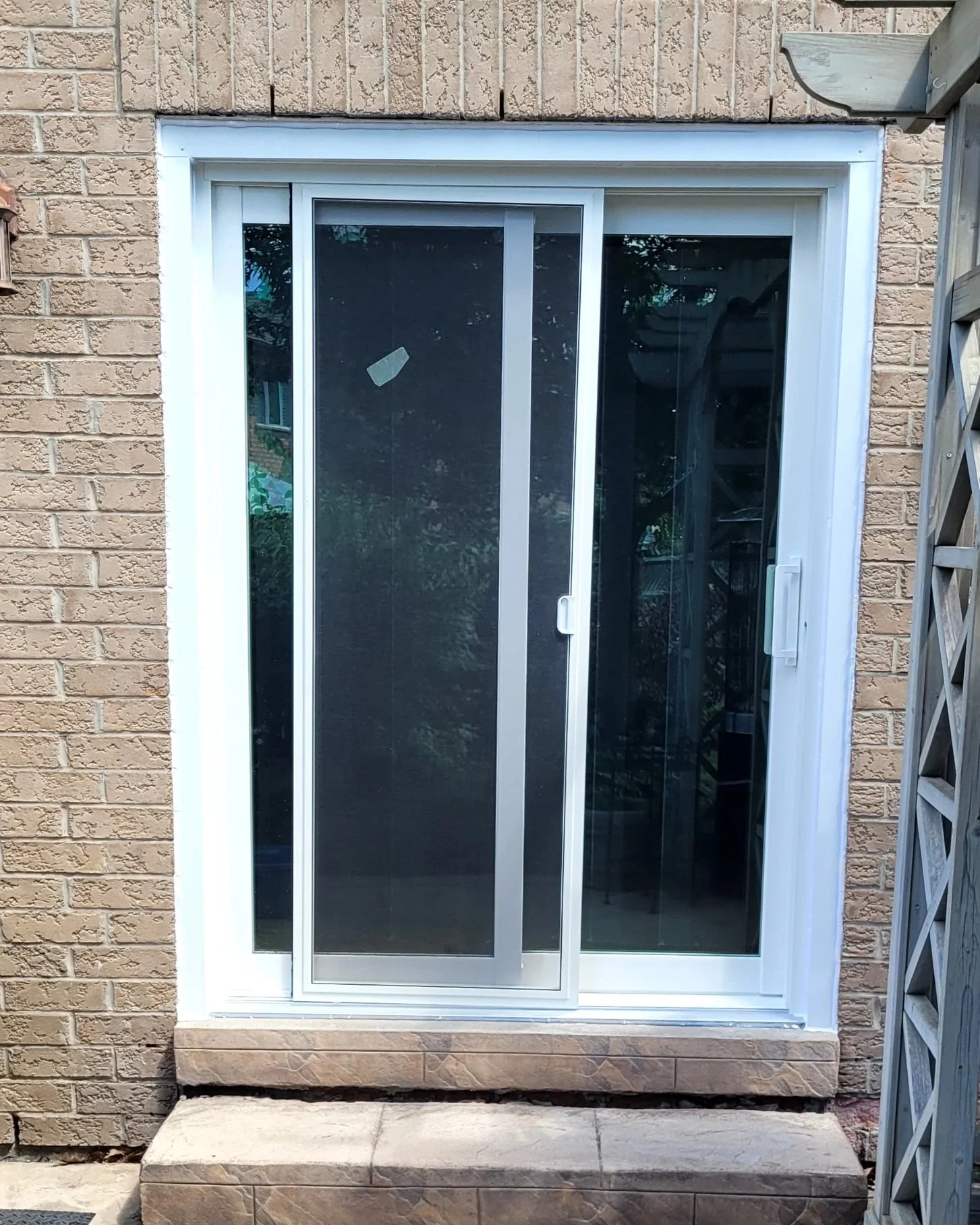 Sliding glass door with a screen door installed, leading to an outdoor area with a brick exterior wall.