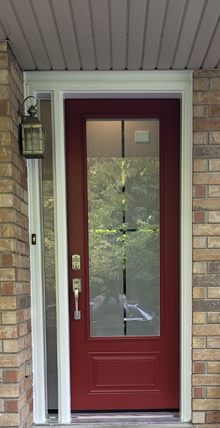 Red front door with a large glass window, white trim, brick walls on either side, and a lantern-style exterior light to the left.