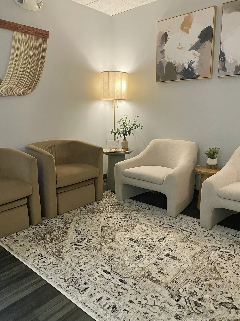 A cozy seating area with four armchairs, a side table, a floor lamp, framed abstract artwork, and a patterned rug.