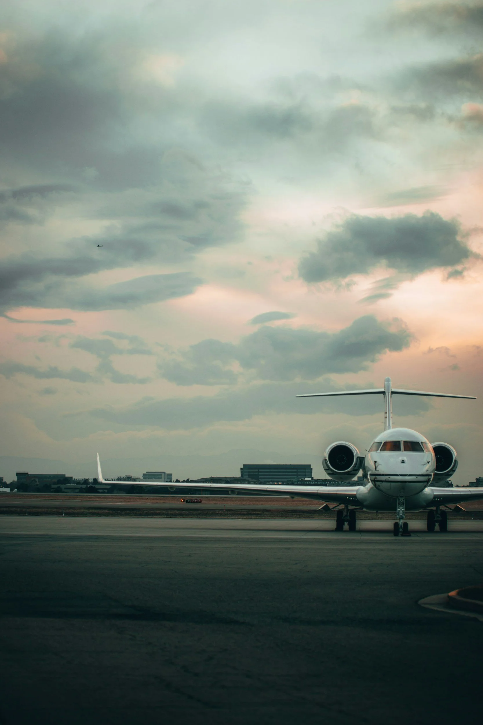 A private jet on the runway at an airport during sunset, with clouds and a cityscape in the background.