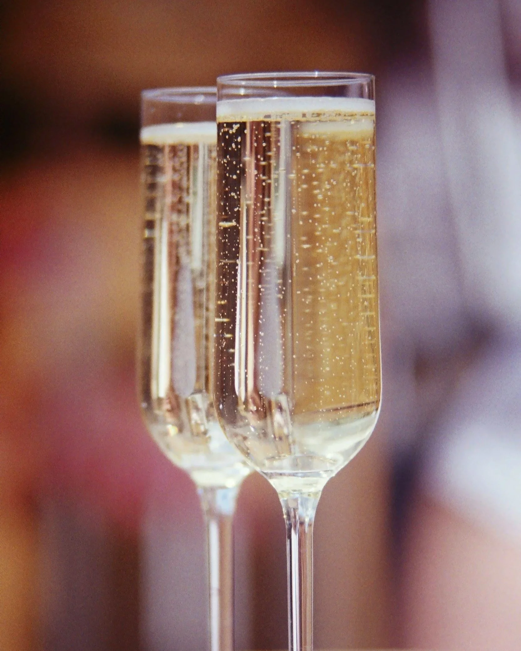 Two champagne glasses filled with sparkling wine, shown close-up with bubbles rising inside, against a blurred background.