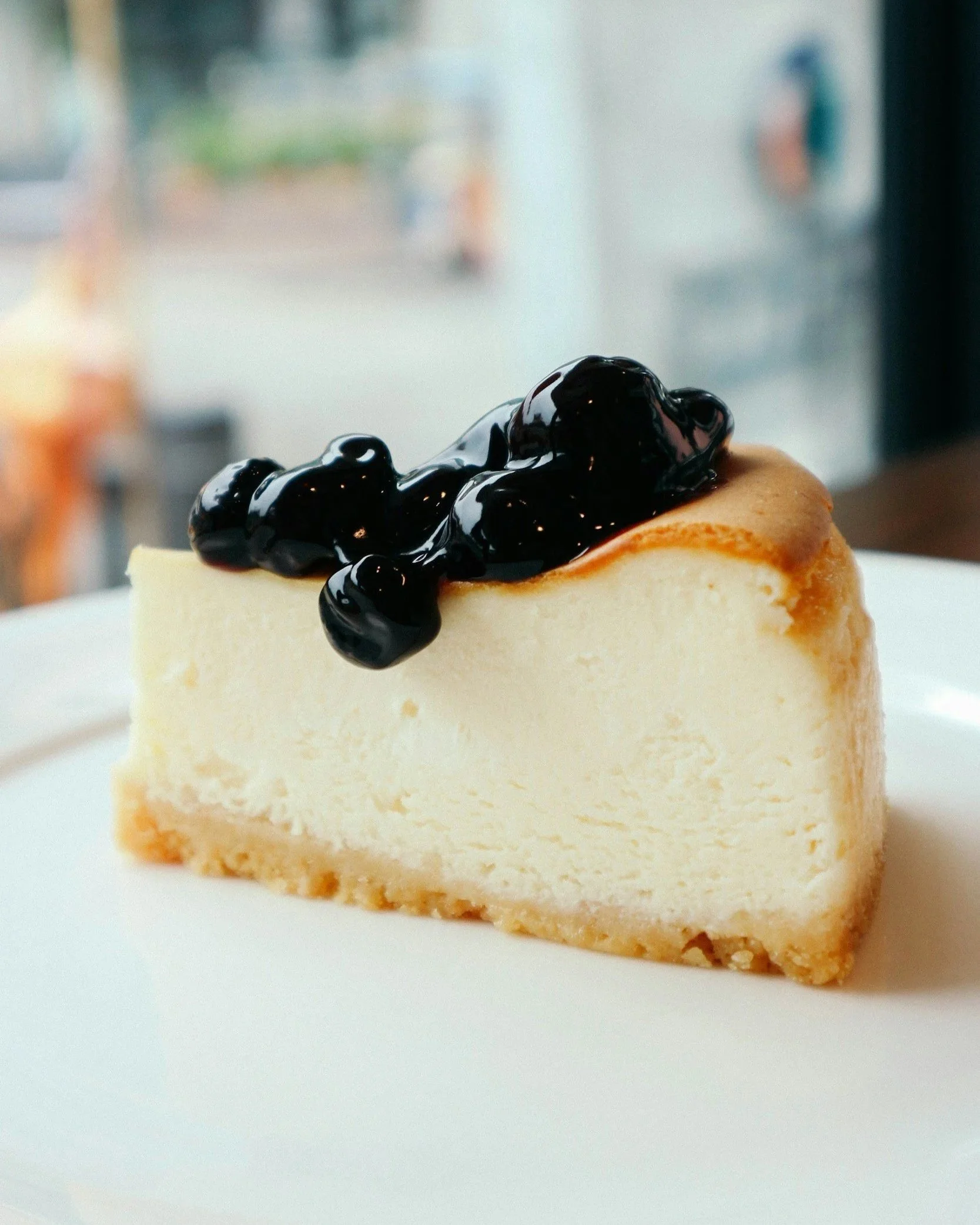 Close-up of a cheesecake topped with blueberry sauce on a white plate with a blurred background.