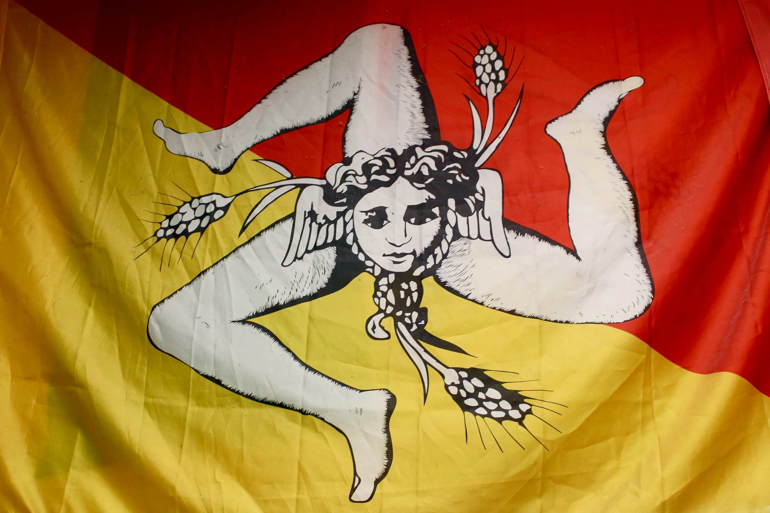 A striking Sicilian banner featuring a diagonally divided red and yellow background with central emblem known as the Trinacria. 