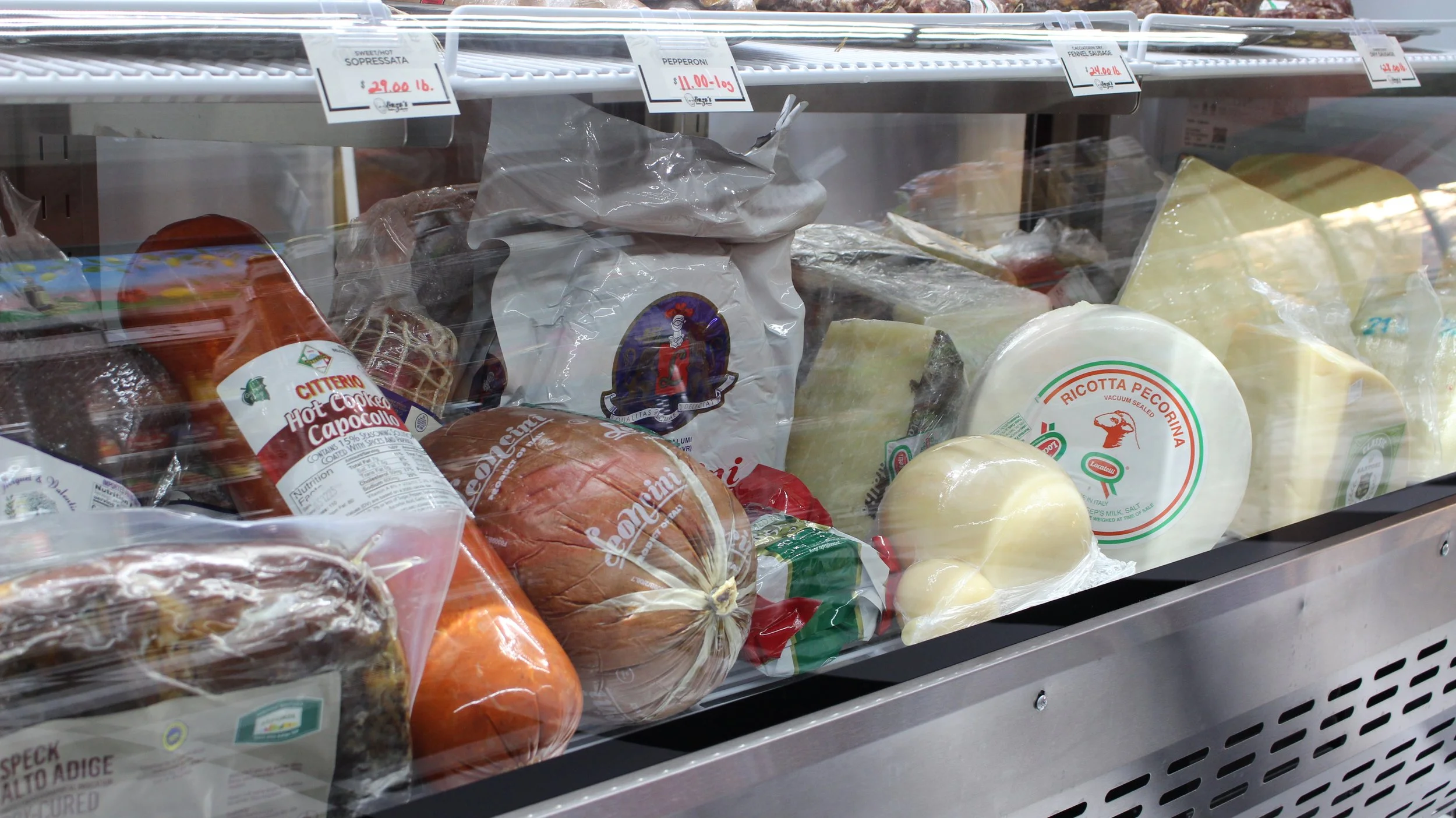 A display case with various cheeses, meats, and deli products.
