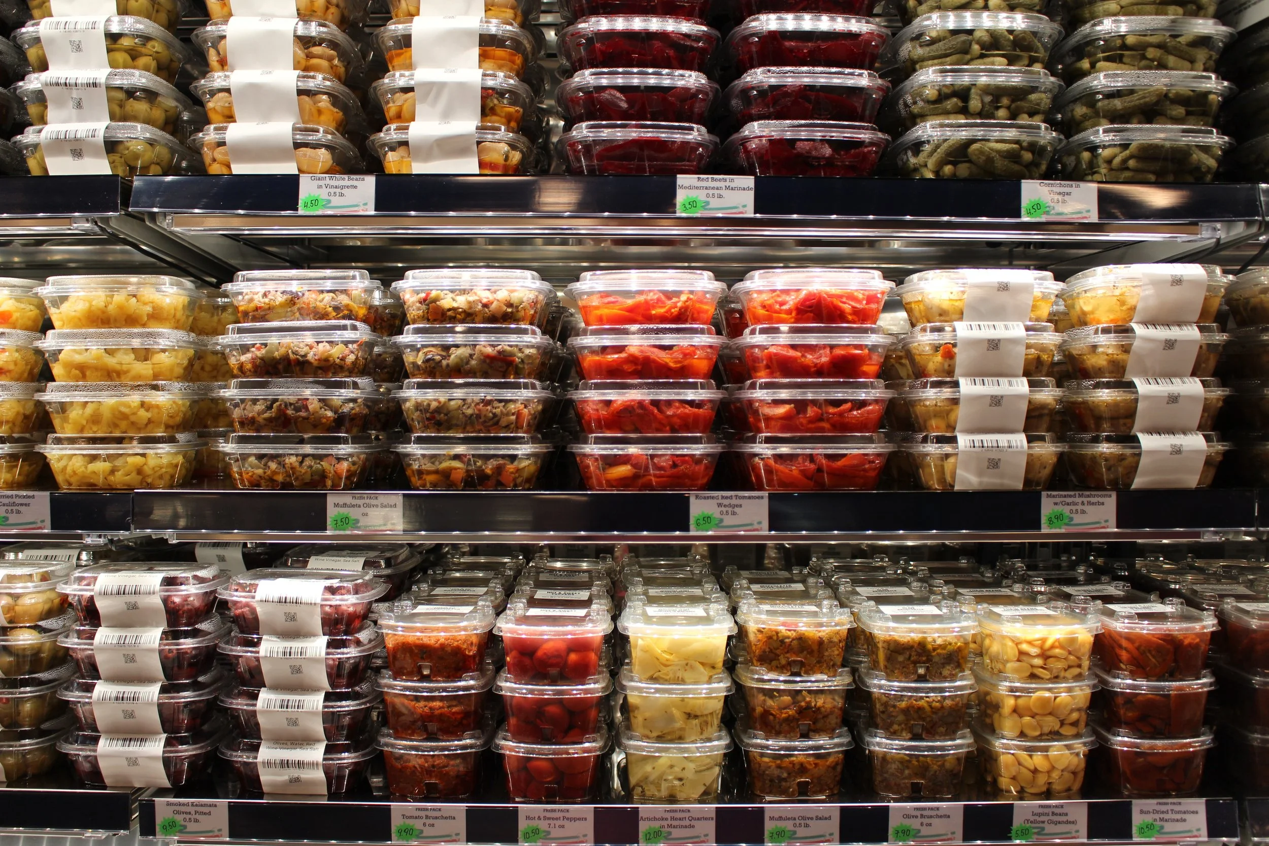 Store shelves stocked with pre-packaged salads, marinated vegetables, and antipasto items in plastic containers.