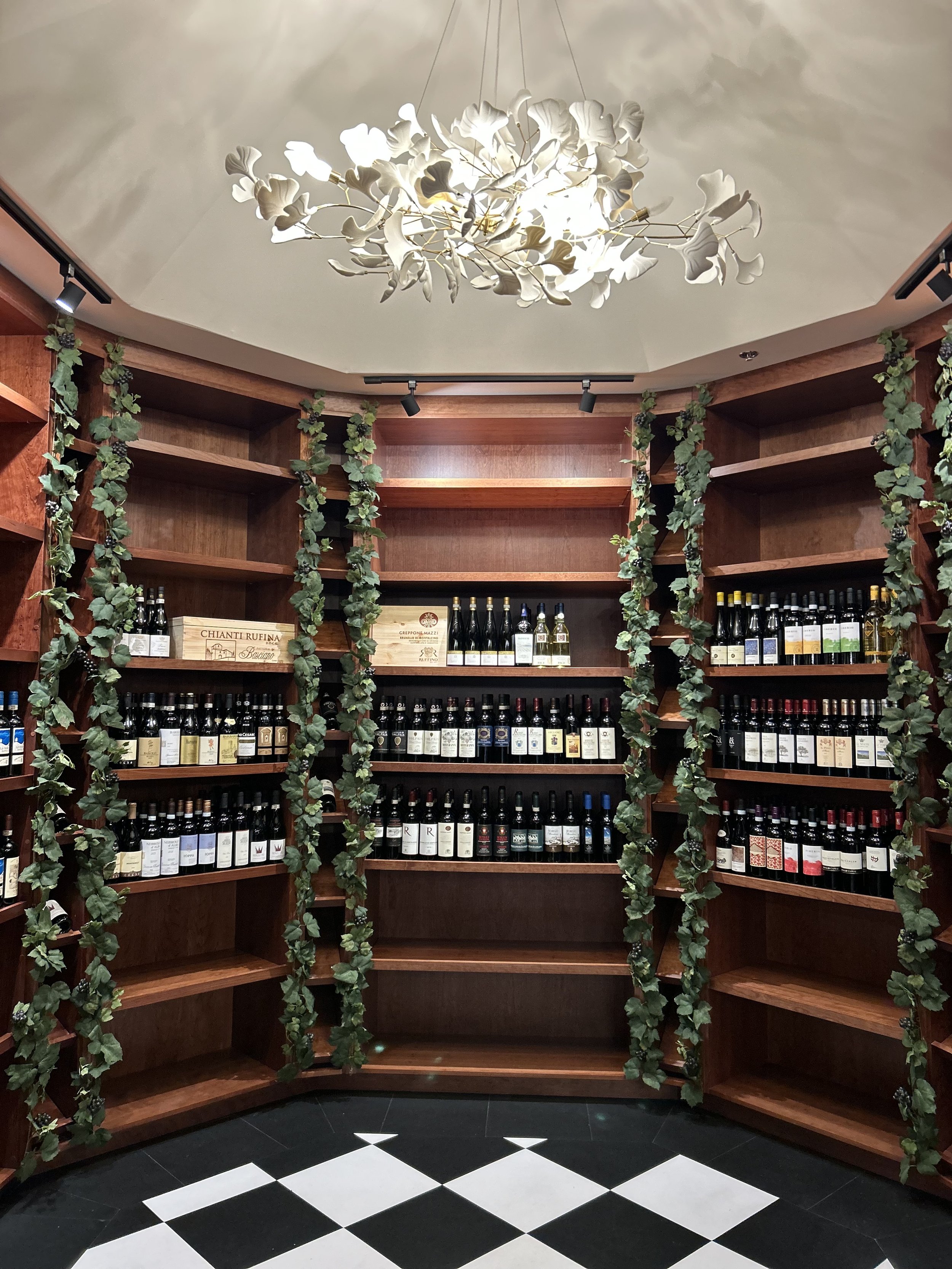 Gallery of Italian wine being displayed in a wooden rotunda surrounded by grape vine decorations. A delicate porcelain chandelier hangs from above. 