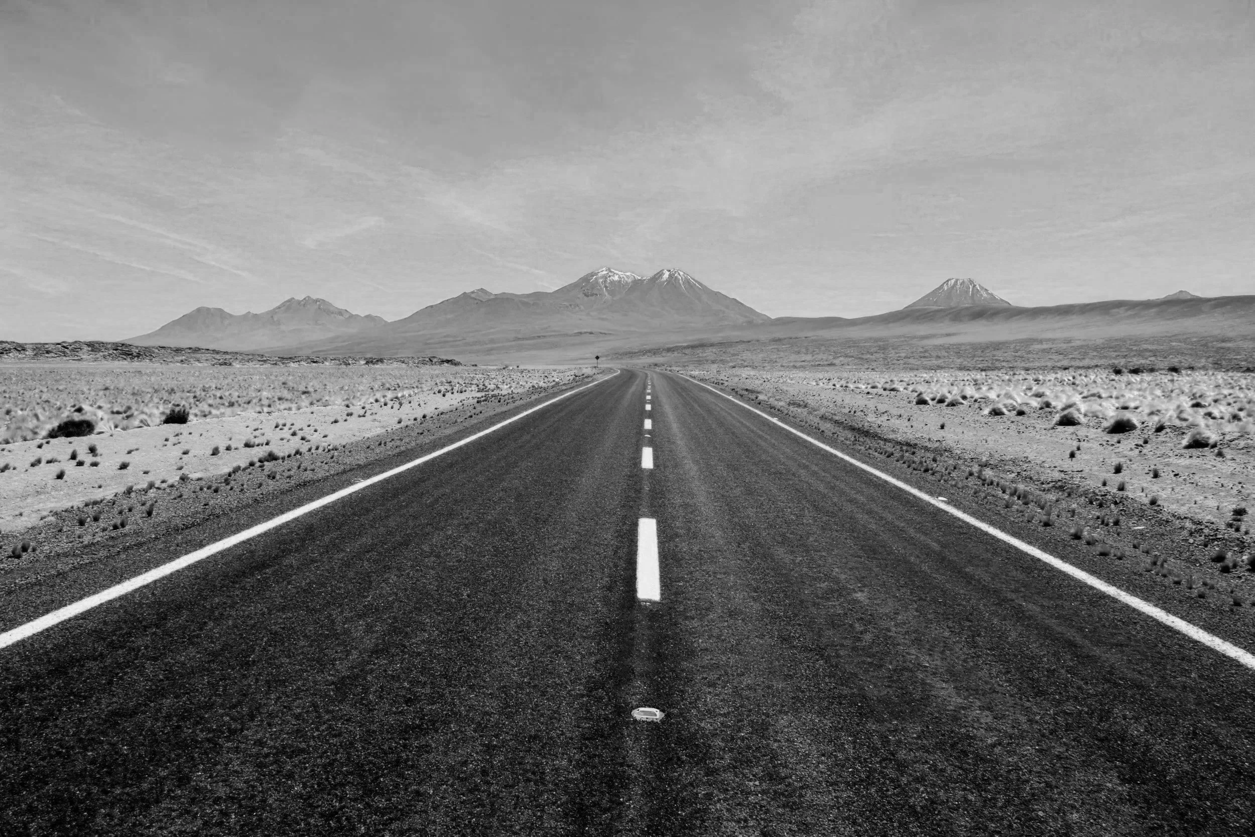 Une route droite dans un désert avec des montagnes en arrière-plan. La photo est en noir et blanc.
