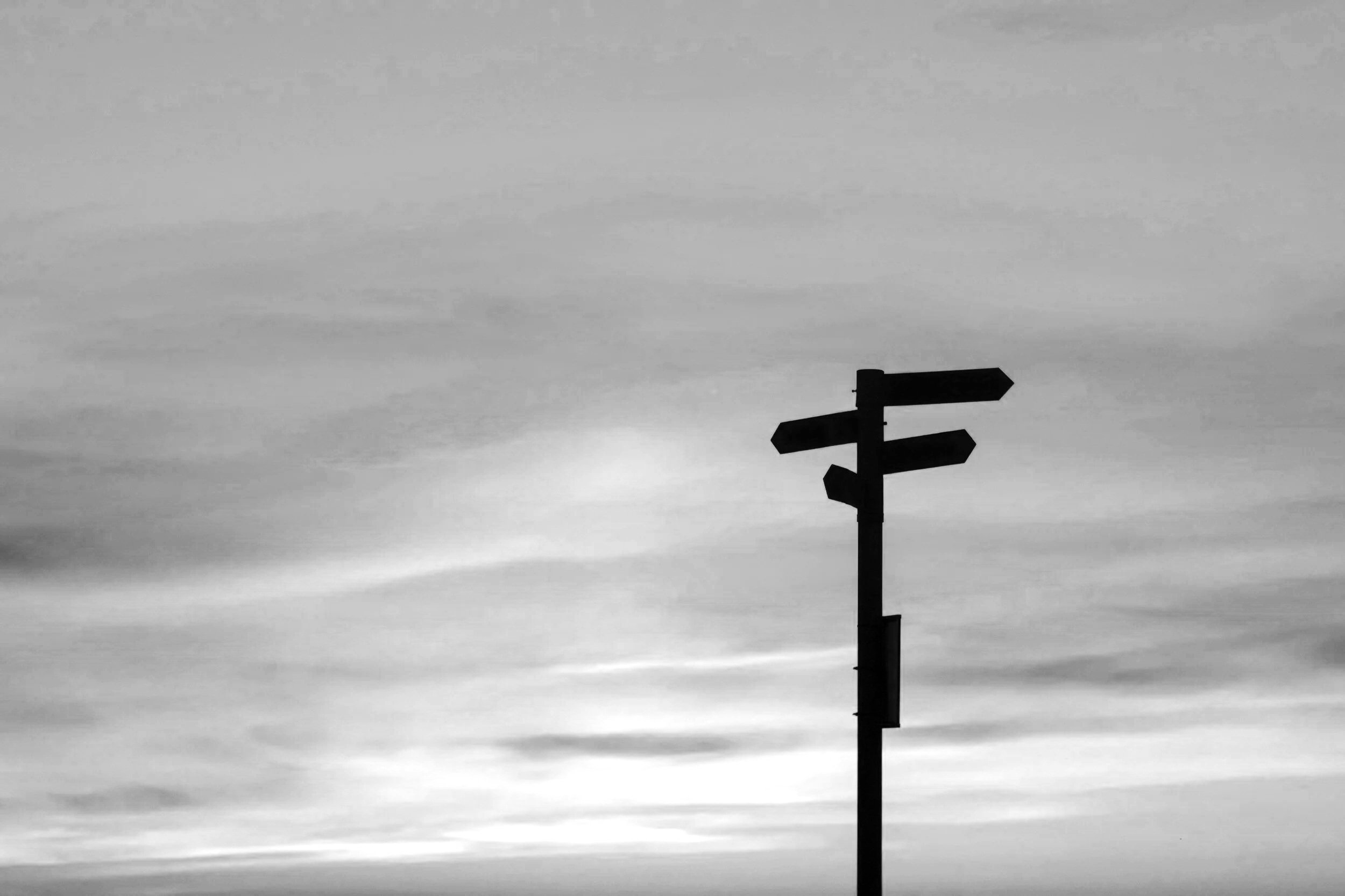 Un panneau de signalisation à plusieurs flèches indique des directions différentes contre un ciel nuageux.