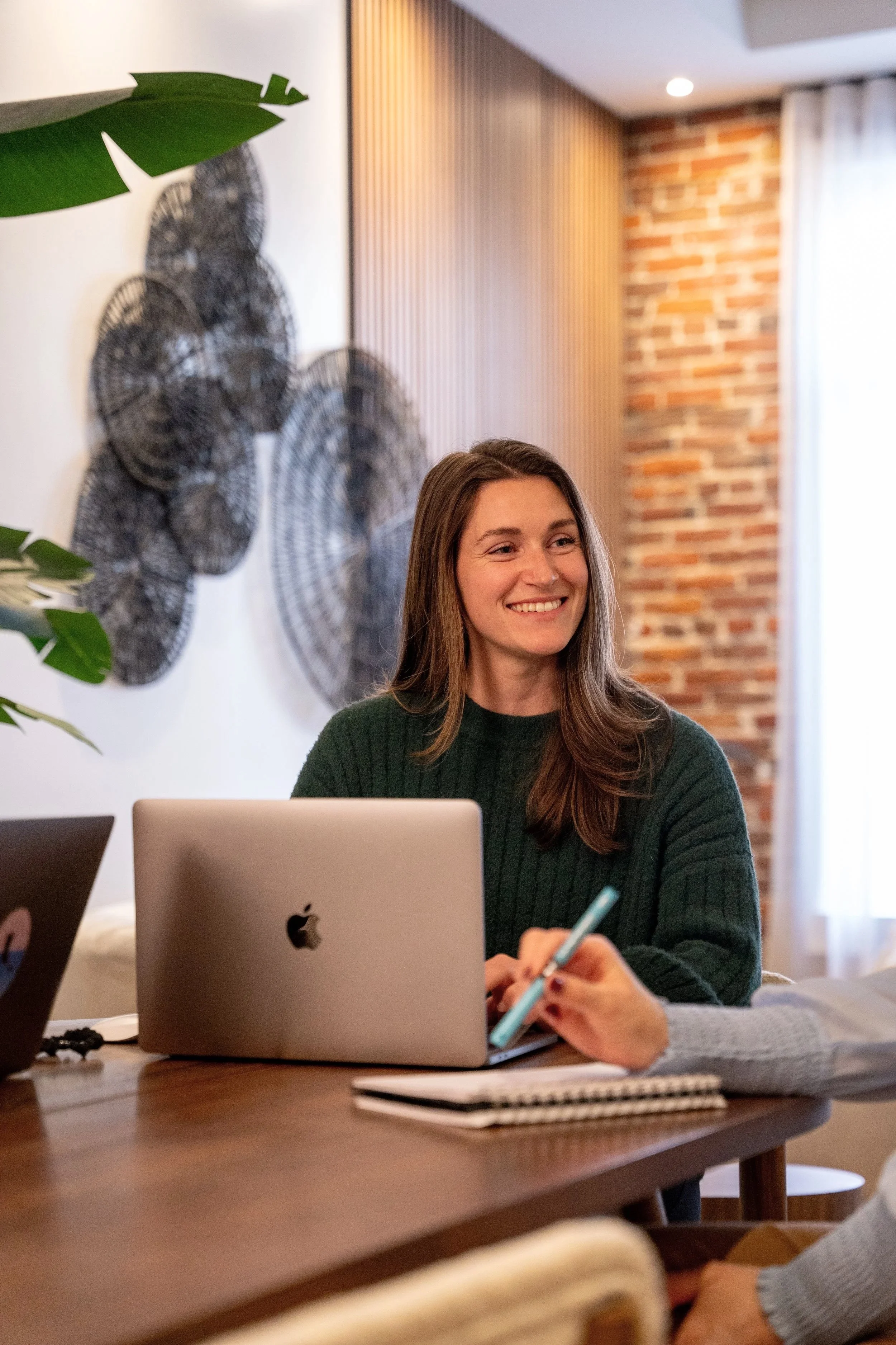 Une femme souriante assise à une table de bureau avec un ordinateur portable Apple