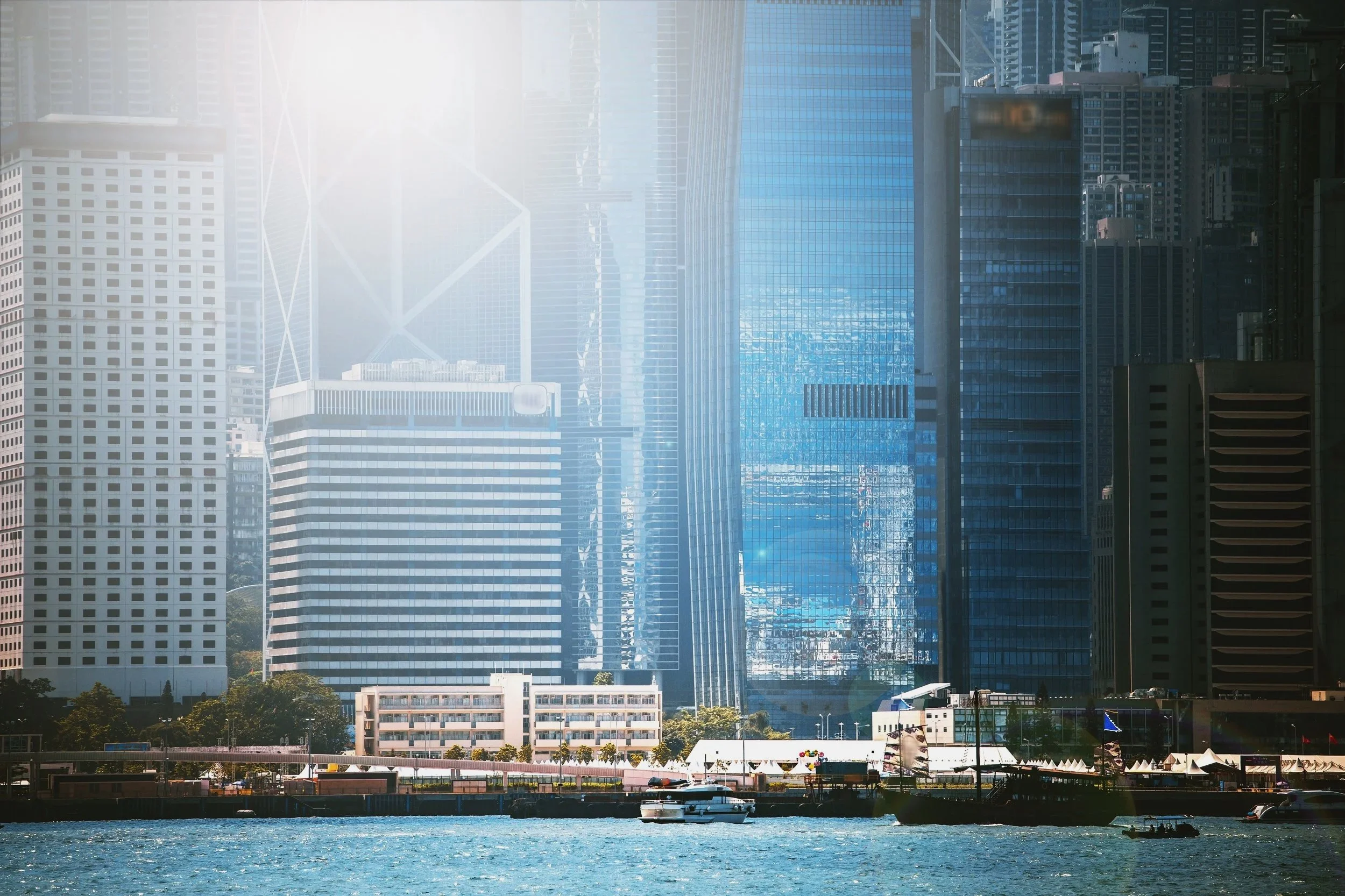 City skyline with tall modern skyscrapers and boats on the water in the foreground.