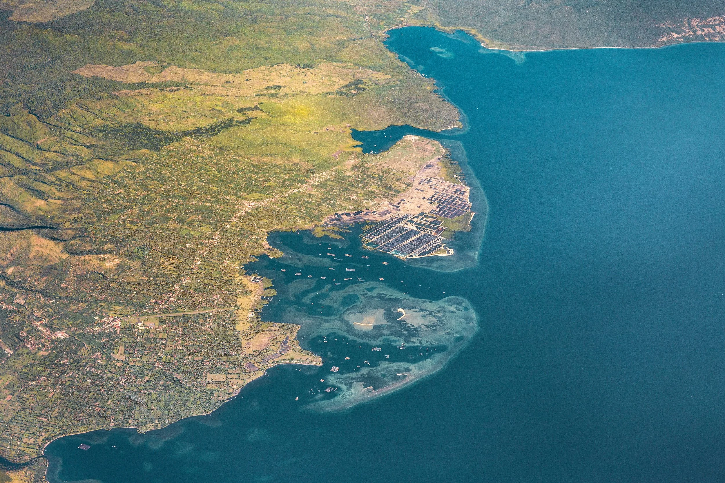 Aerial view of a coastal area featuring a large body of water, wetlands, and agricultural fields with a grid-like pattern.