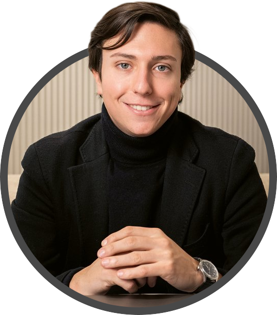 Andrea Posa wearing a black turtleneck and blazer, smiling with hands clasped on a table, in an indoor setting.