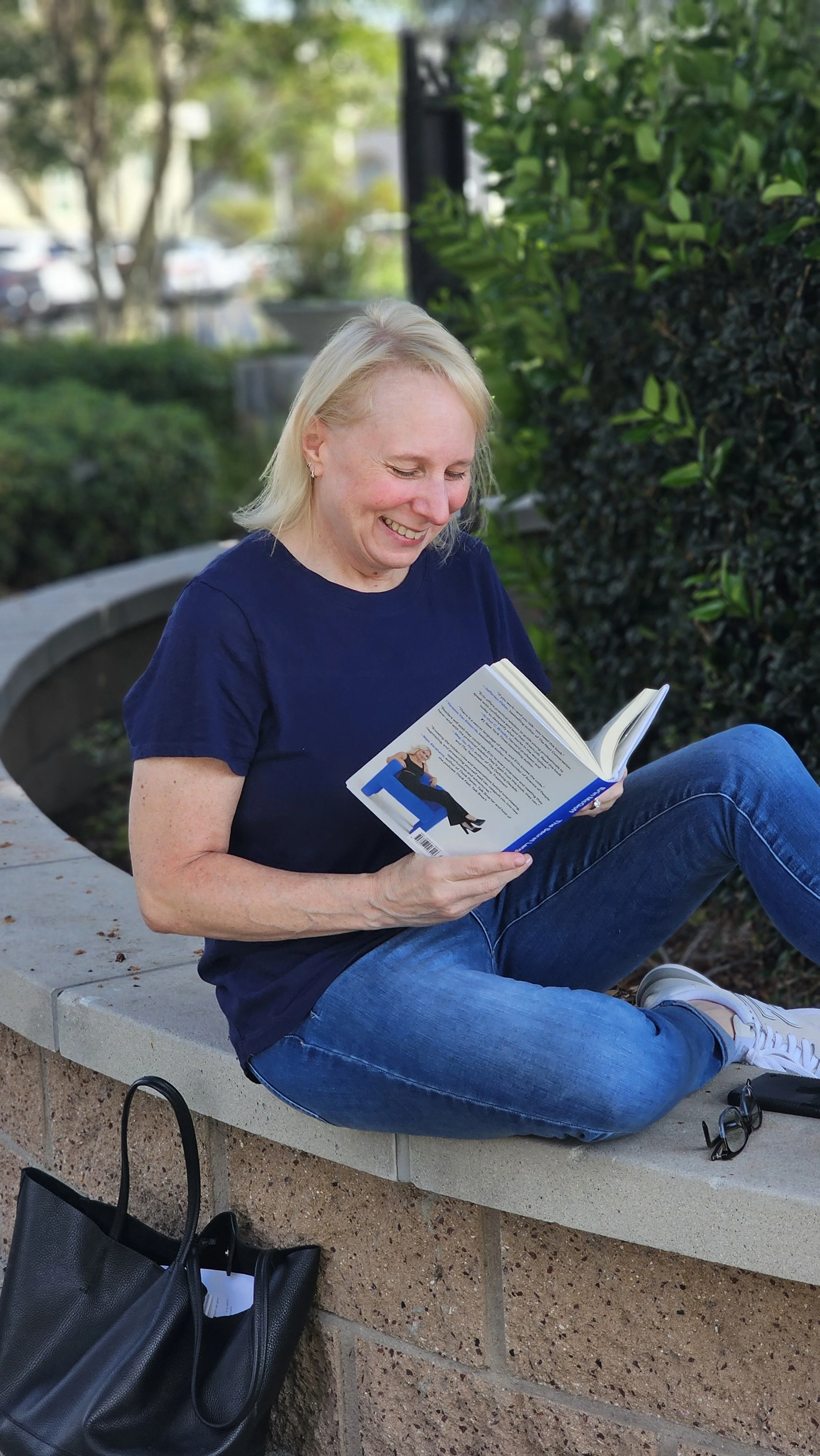 Jennifer Schecter, founder of Schecter Solutions, seated outdoors reading and laughing