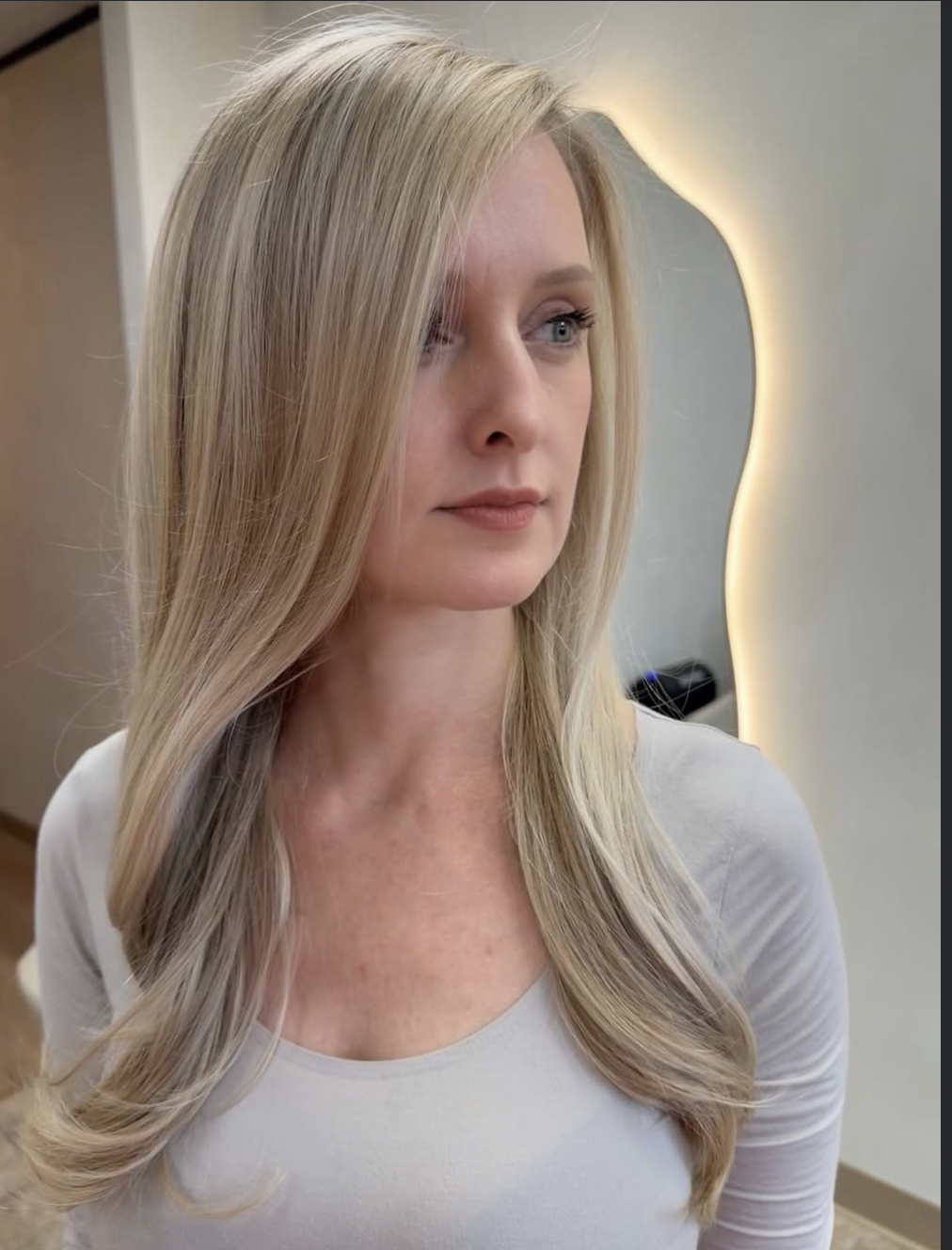A woman with long blonde hair looking to the side in a salon or spa setting.