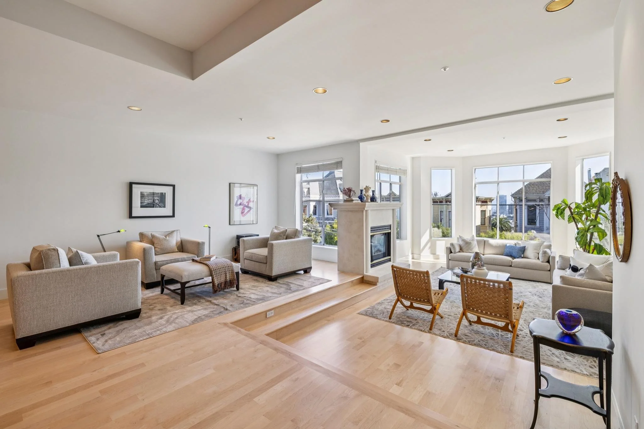 Bright living room with multiple sofas, a fireplace, large windows, and hardwood flooring.