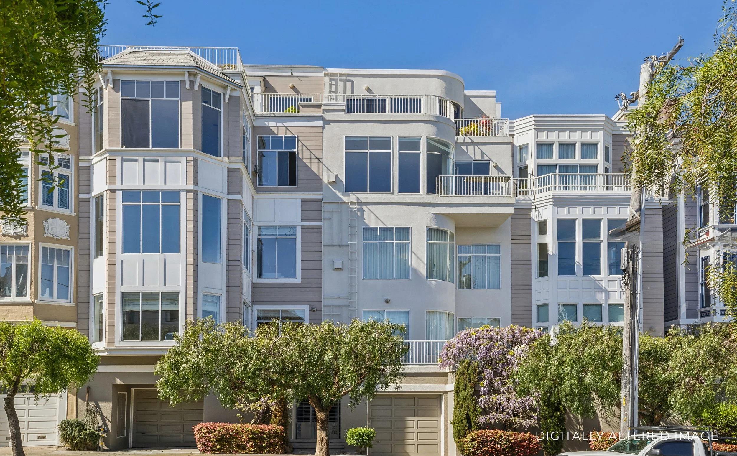 Multi-story apartment building with bay windows, balconies, and a garage, surrounded by trees and shrubs, under a clear blue sky.