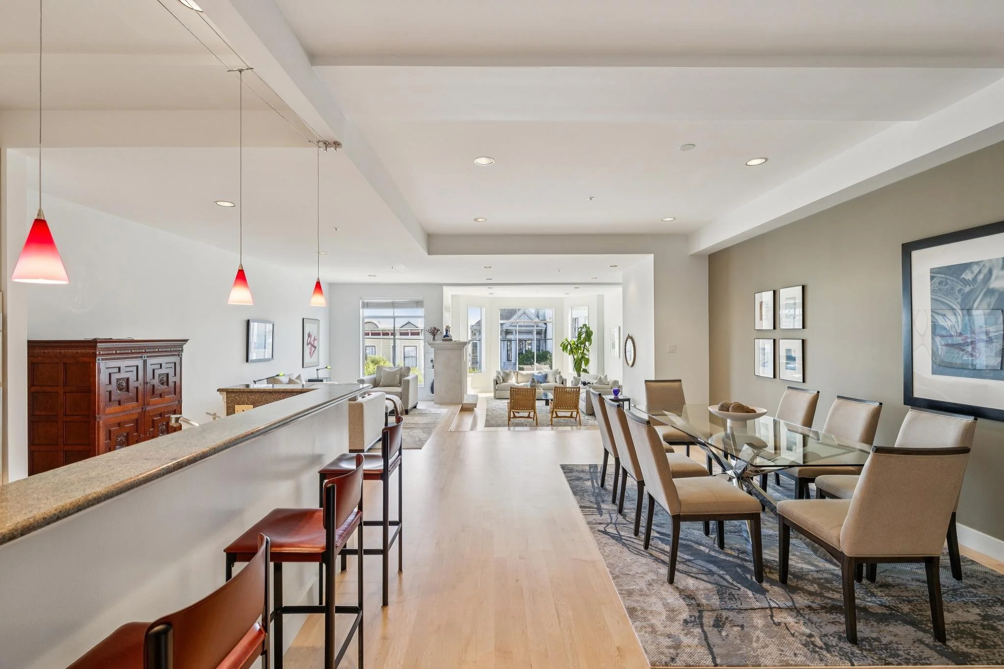Open-concept living and dining area with large windows, beige walls, wooden flooring, a glass dining table with beige chairs, and a cozy sitting area with white sofas and armchairs near the windows.