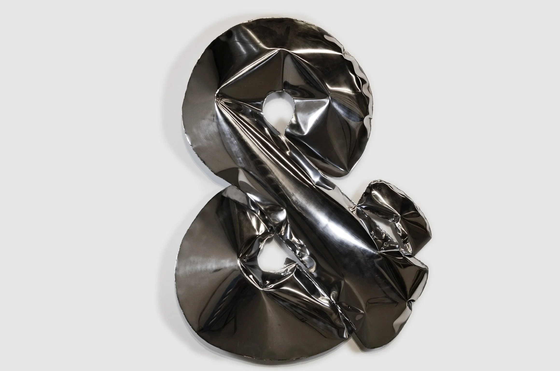 A metallic sculpture resembling a lowercase letter 'a', made from crumpled, reflective metal material.