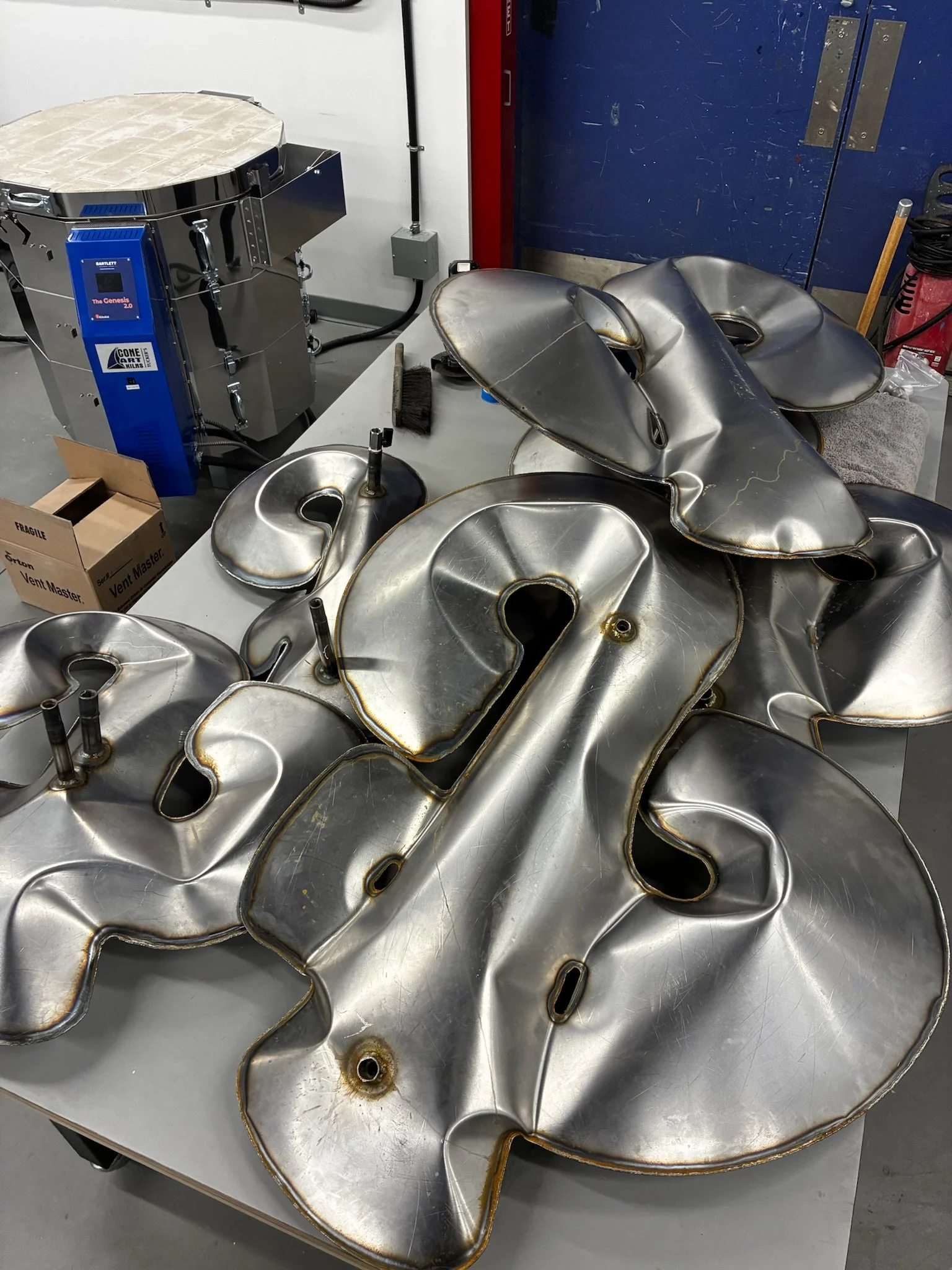 Large metal sign with shiny surface and cut-out letters, lying on a table, with a forming machine in the background.